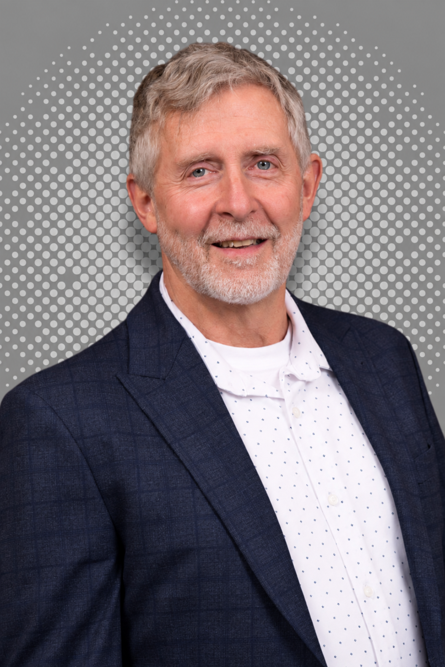 Elderly man in suit jacket with polka dot shirt posing against dotted background.