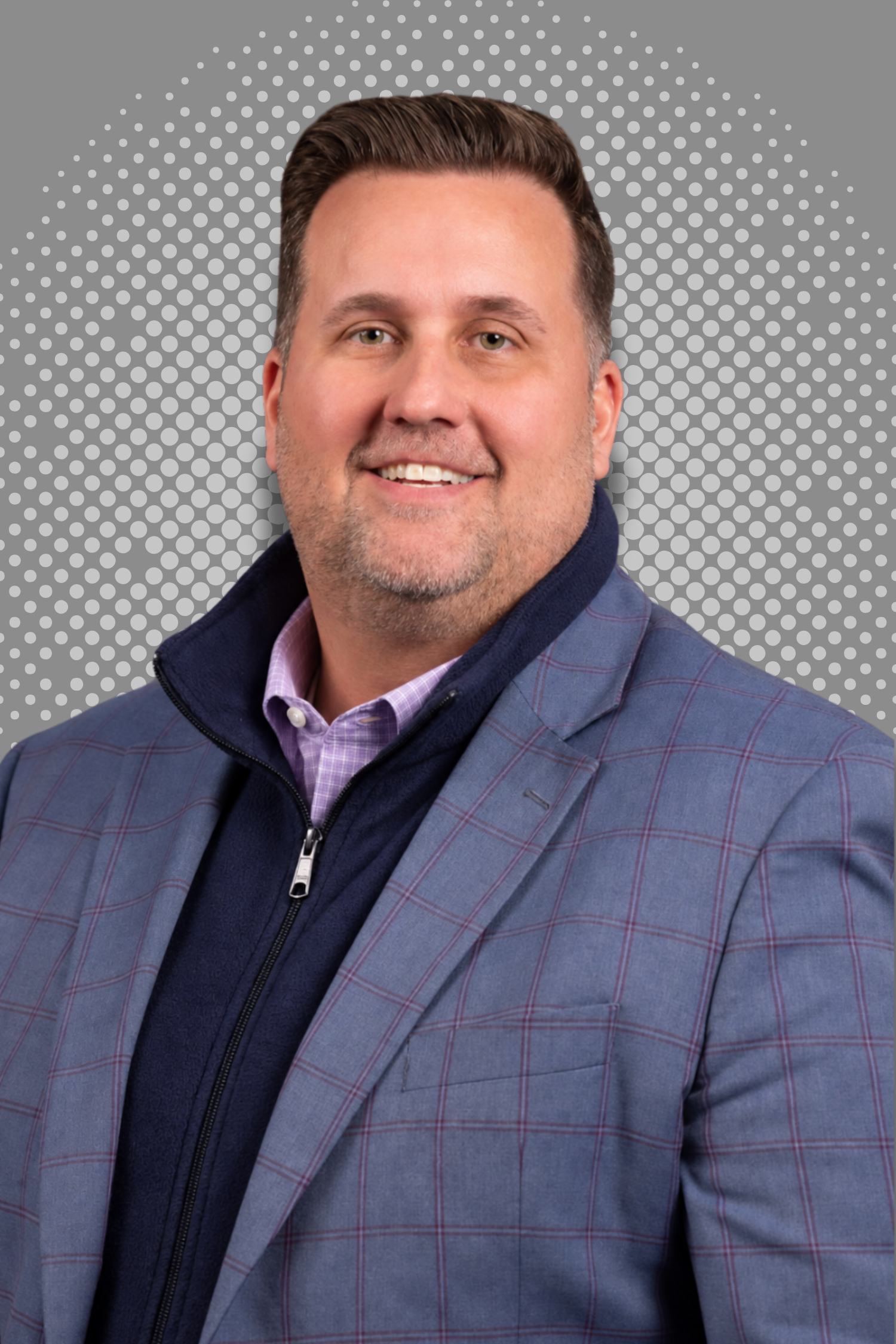 Man wearing a checked suit and dark sweater with a dot-patterned background.
