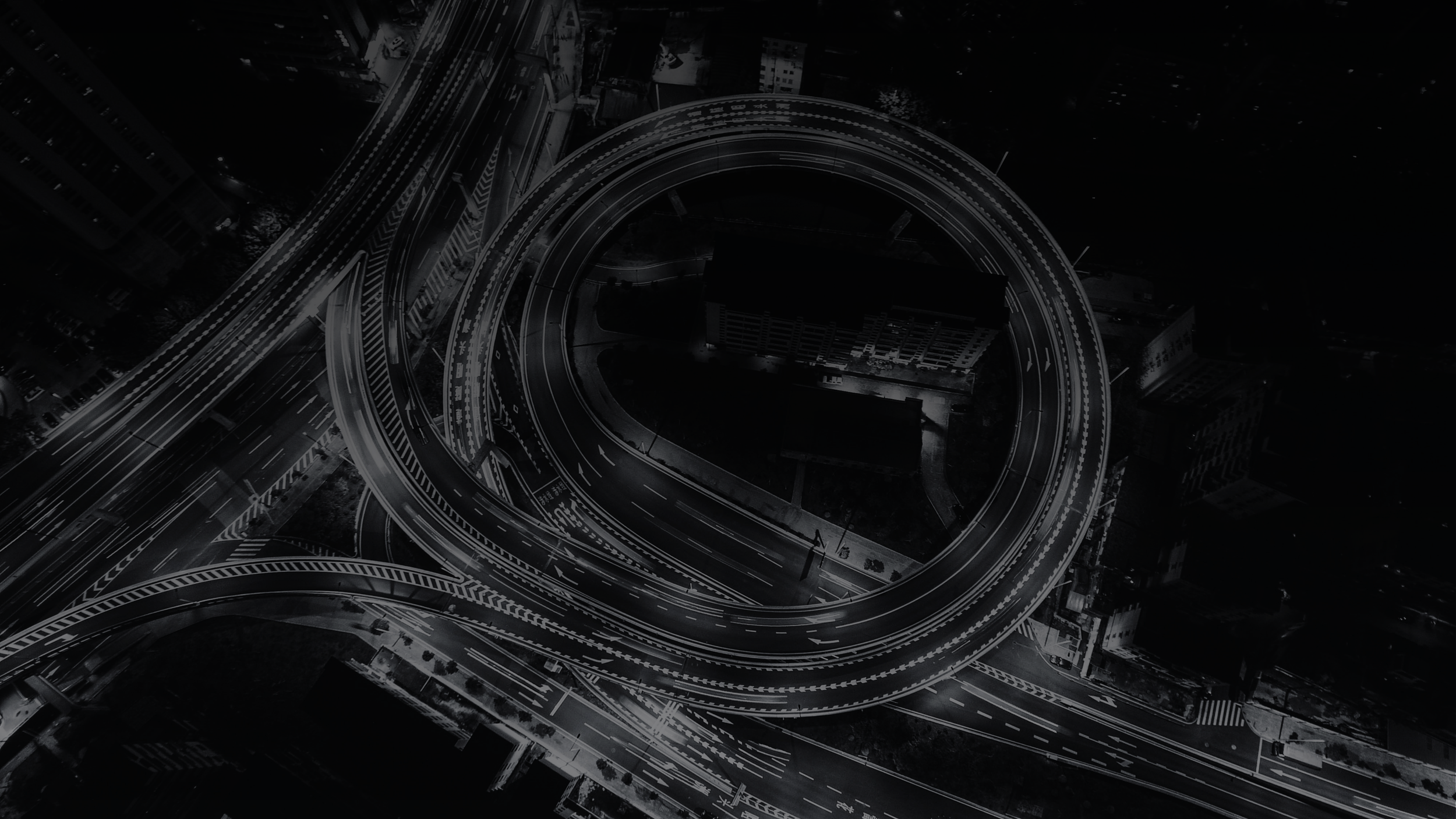 Aerial view of a complex highway interchange at night with cars, surrounded by tall buildings.