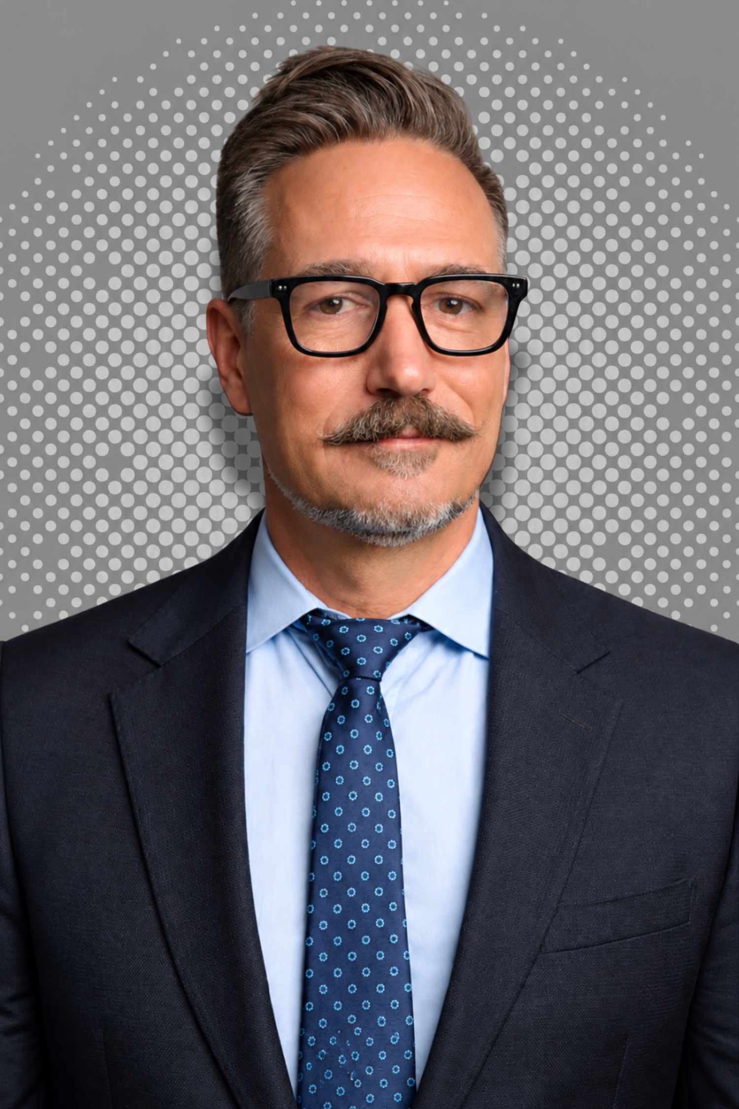 Man wearing glasses, navy suit, and white shirt against a gray dotted background.