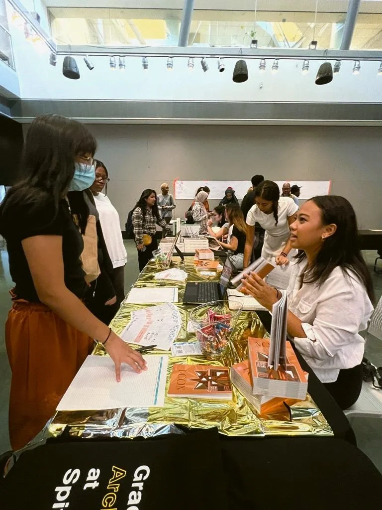 People at a table in a large indoor event space, some looking at documents and laptops, engaging in a discussion or registration process.