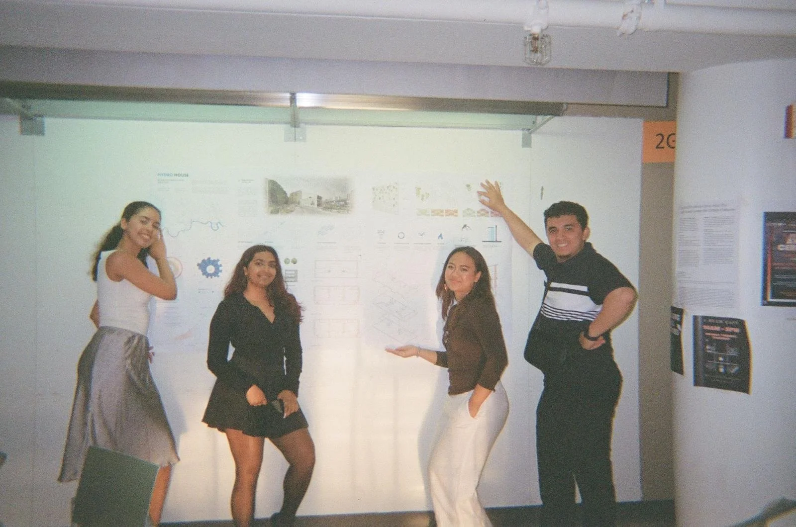 Four young people standing in front of a wall with posters, smiling, and posing for the photo.