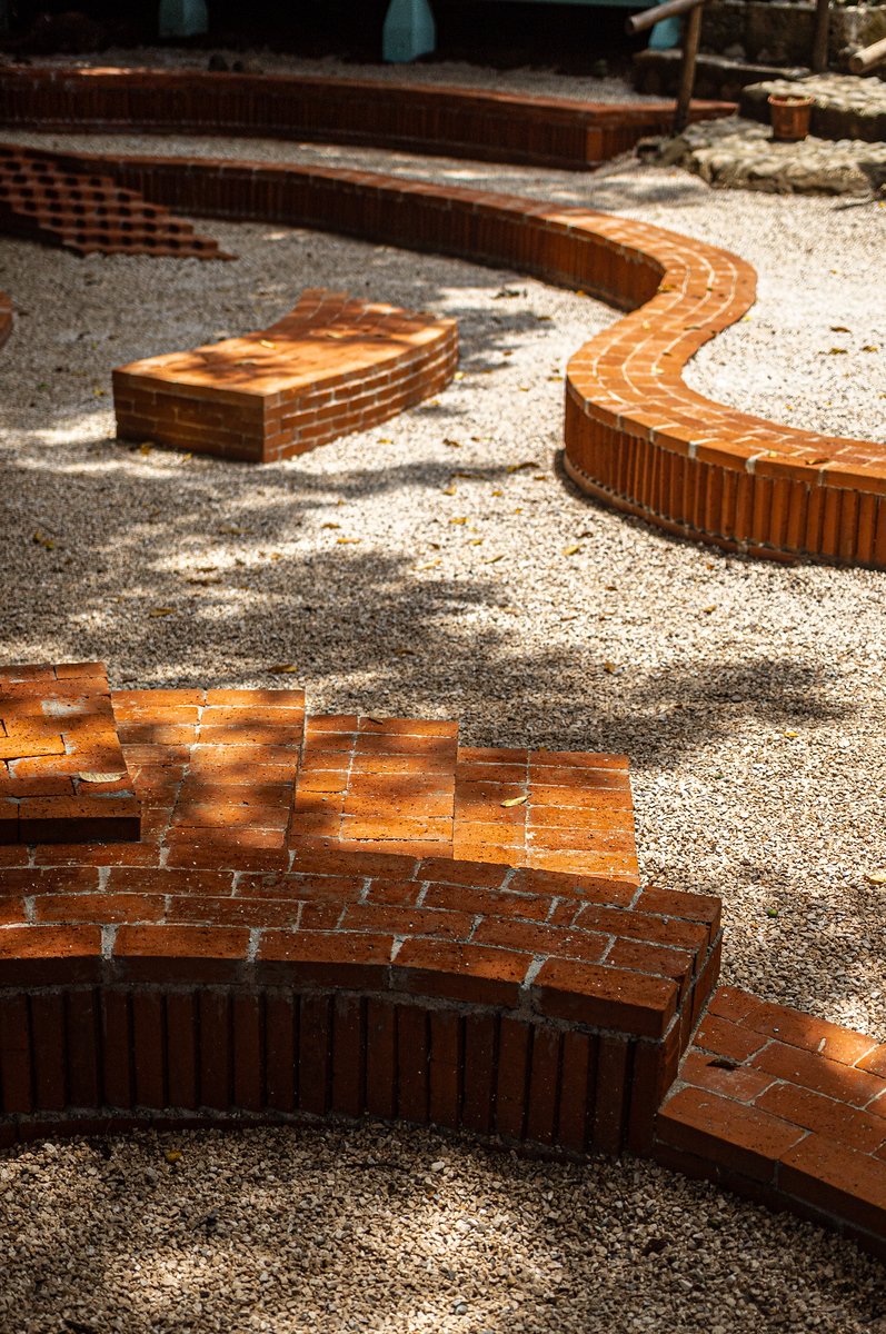 Curving brick benches and pathways in a garden area with gravel ground and shaded by trees.