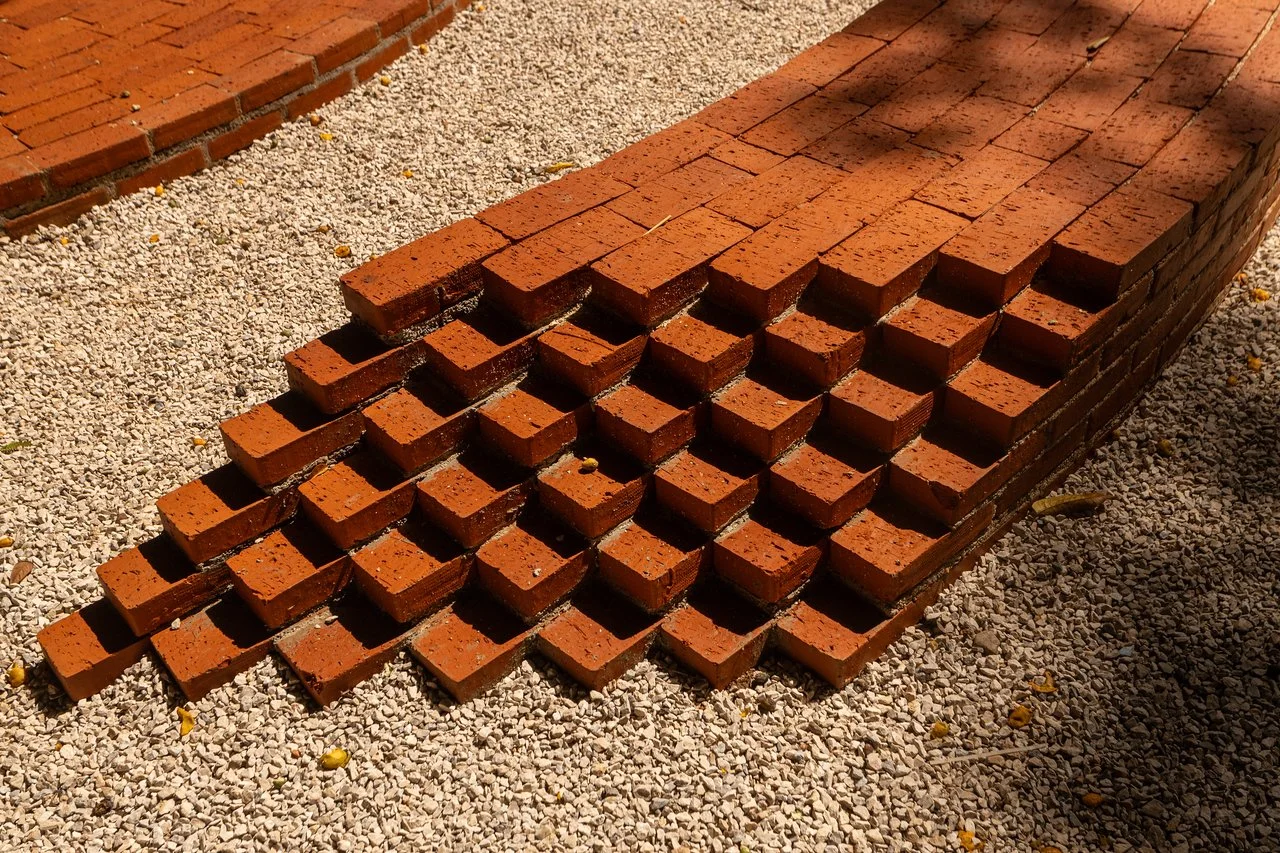 Stack of red bricks arranged in a stepped pattern on a gravel surface.