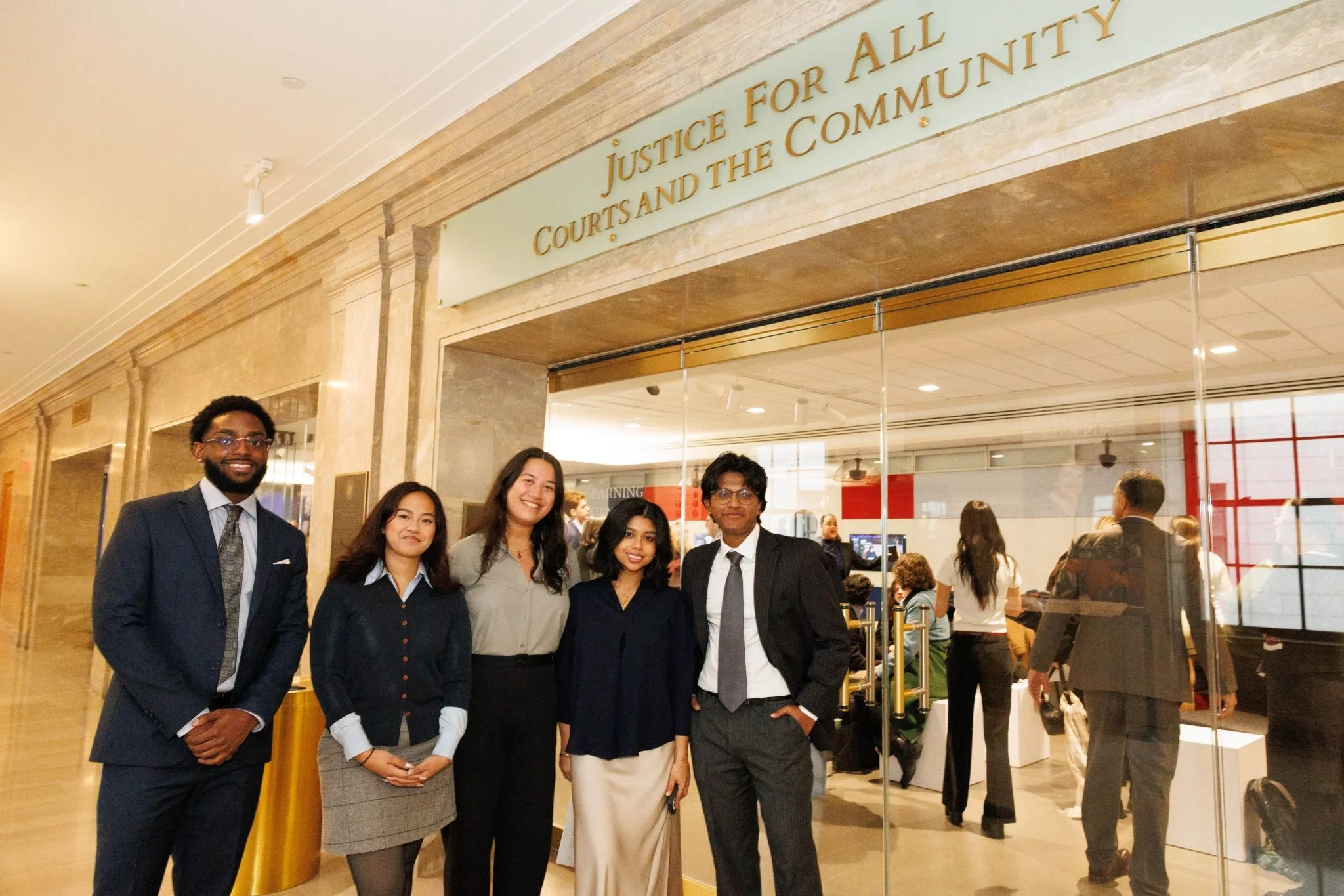 Group of five people in formal attire standing outside a courthouse with a sign that reads 'Justice for All Courts and the Community.'