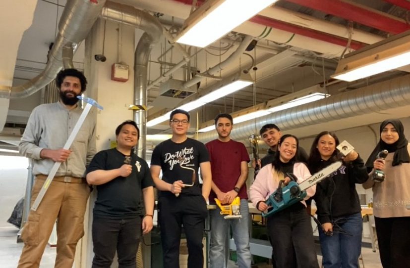 Group of eight diverse young adults working in a workshop with tools and equipment.