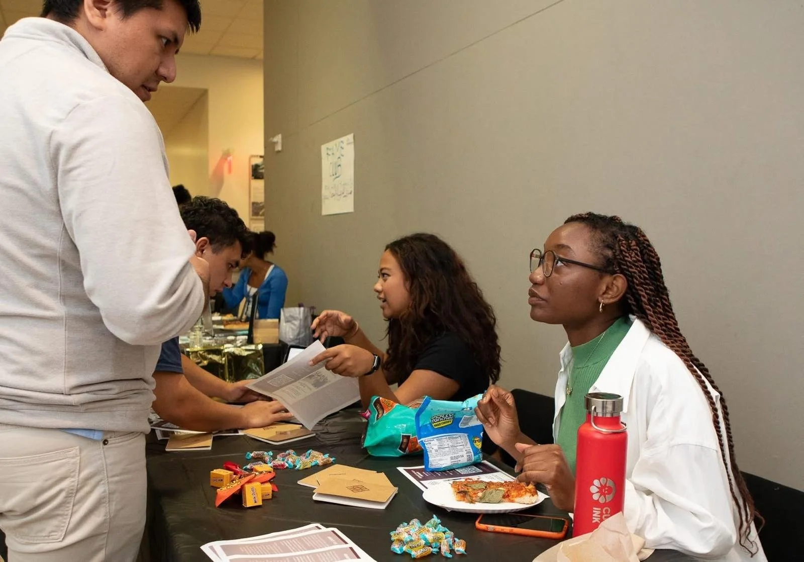 People at a table with candy, snacks, and documents, engaging in conversation.