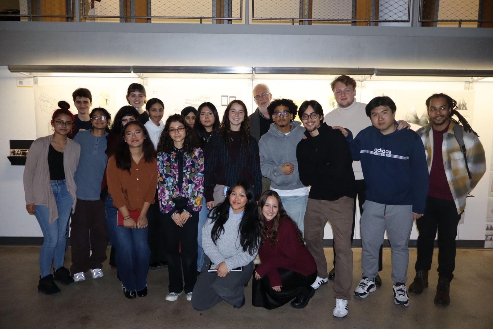Group of diverse young adults and an older man posing together indoors in front of a white wall.