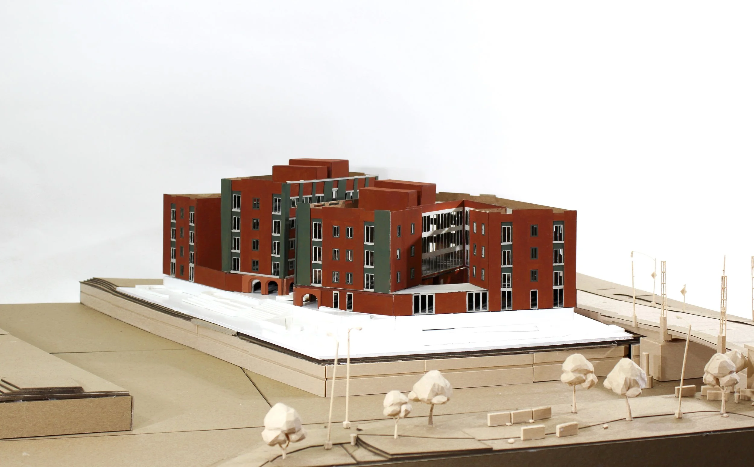 Architectural model of a multi-story building with brick and green exterior, surrounded by scaled trees and street elements.