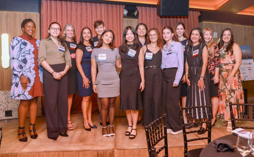 Group of women standing together on a stage at a professional event or conference, smiling for the photo.