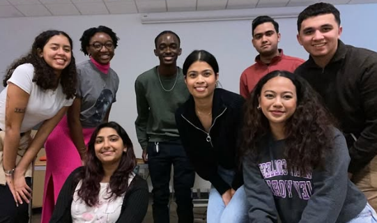 Group of eight diverse young adults smiling and posing together indoors.