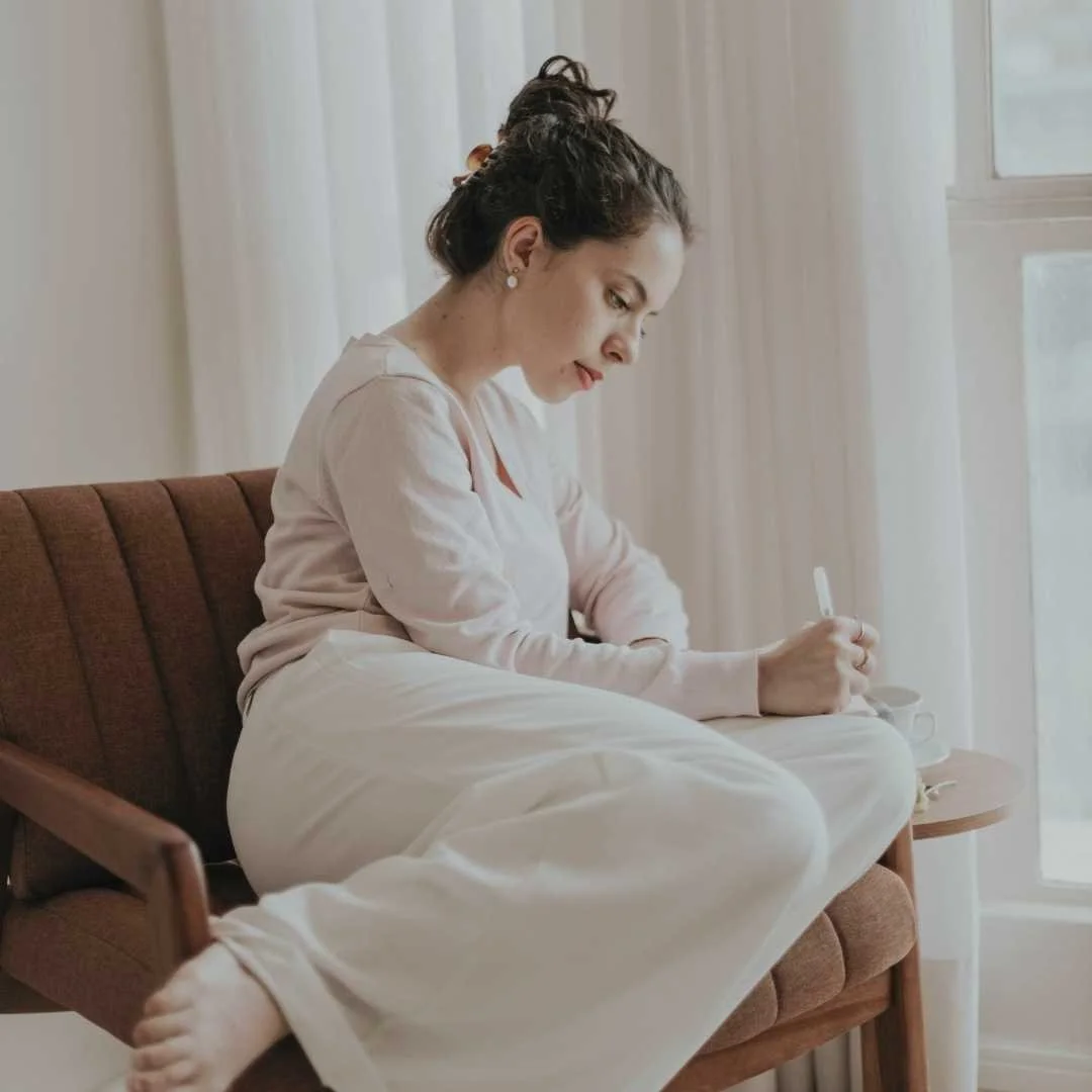 Person sitting in a chair writing in a notebook, representing reflection or journaling between therapy sessions.