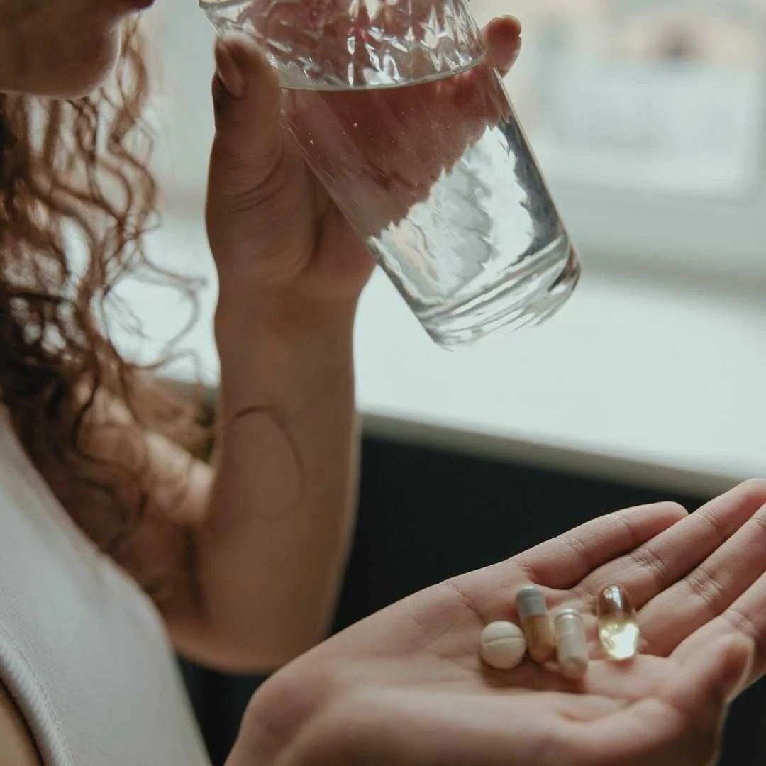 Person holding several pills in one hand and a glass of water in the other, representing medication tracking as part of mental health care.