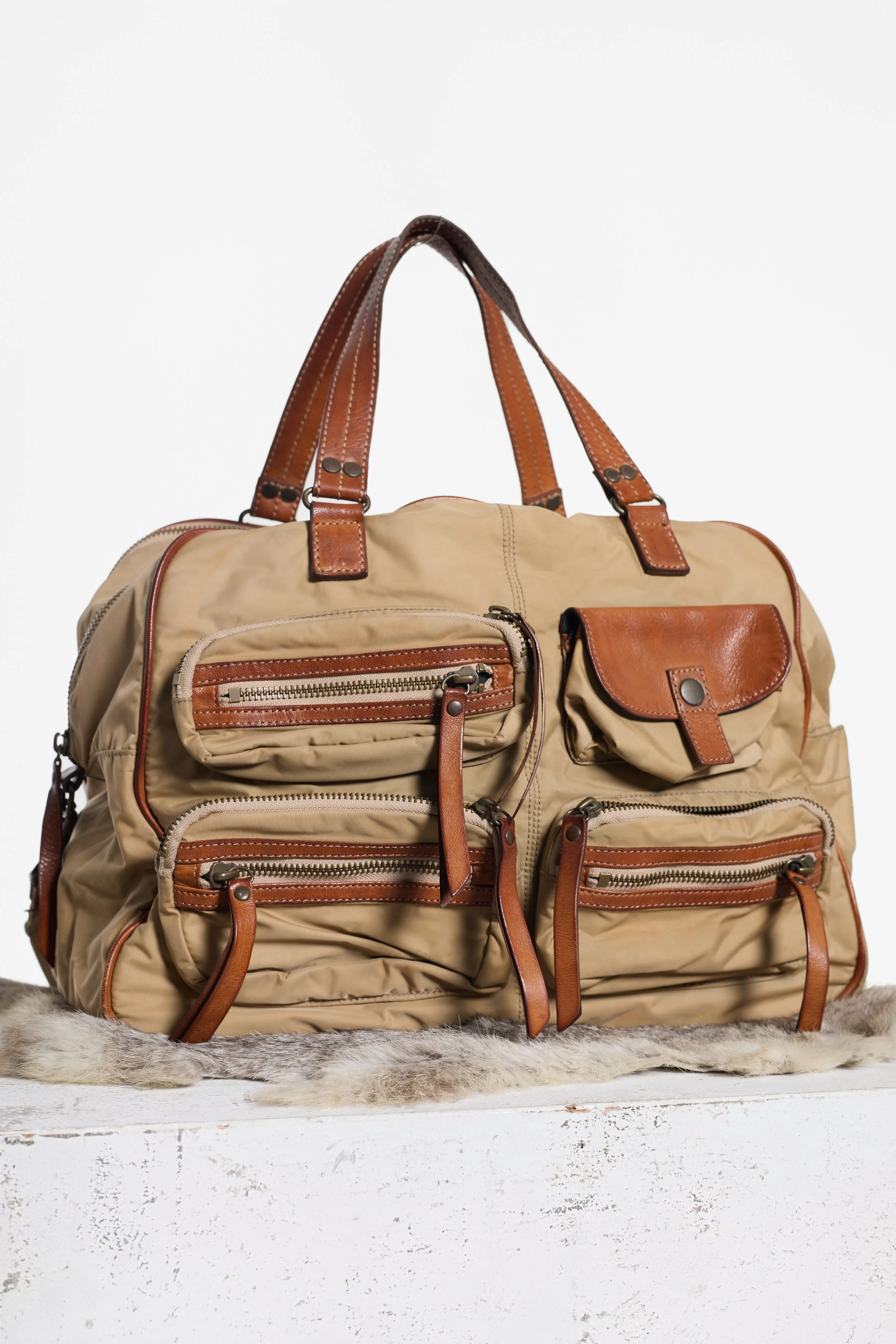 Khaki utility tote with brown leather trim and exposed metal zips