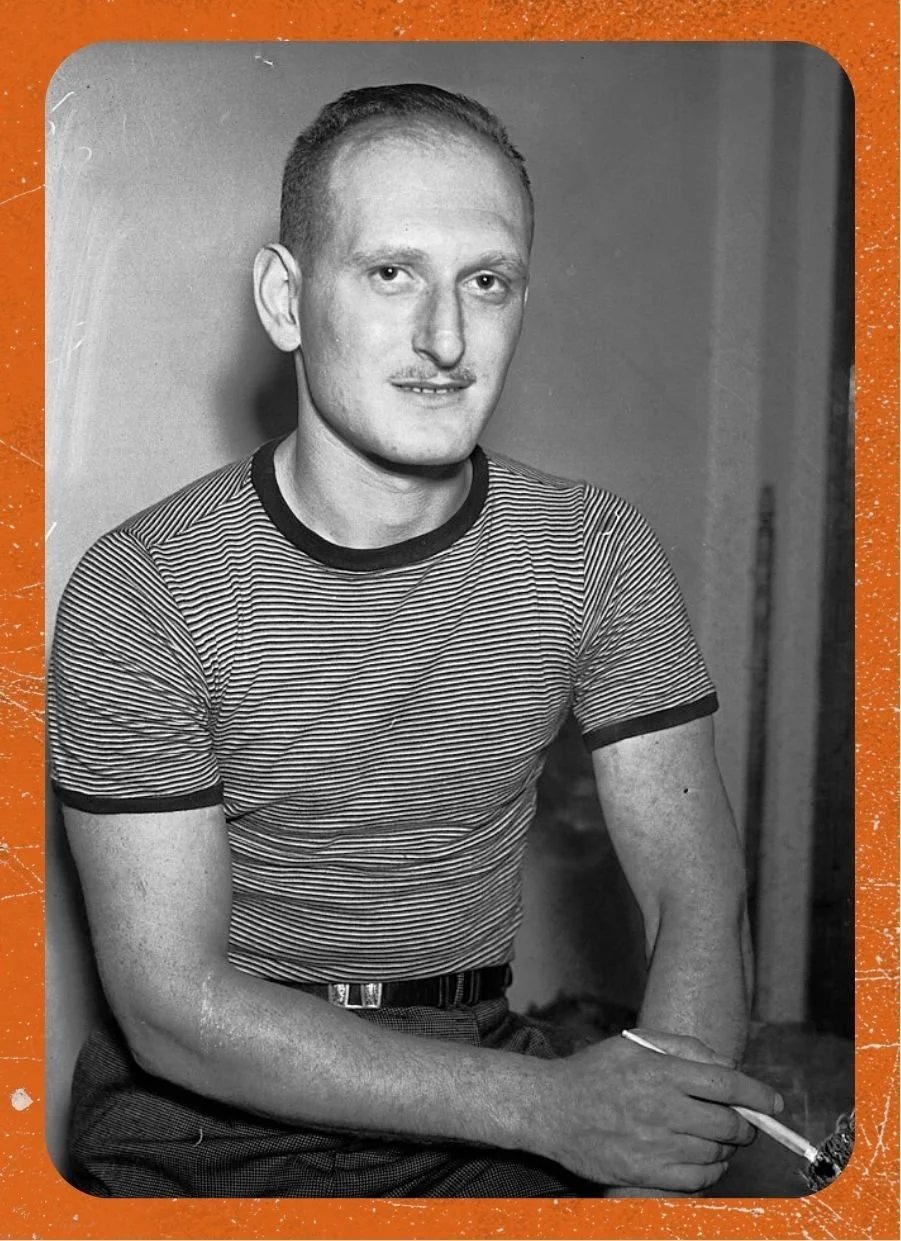 Sidney Franklin appears to sit, off-center to the left, as he poses for the camera. He dons a horizontally-striped ringer tee. He loosely crosses his arms in front of him as he gazes towards the camera.