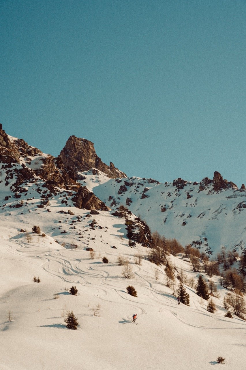 Snow-covered mountain landscape with ski tracks and a skier in red gear