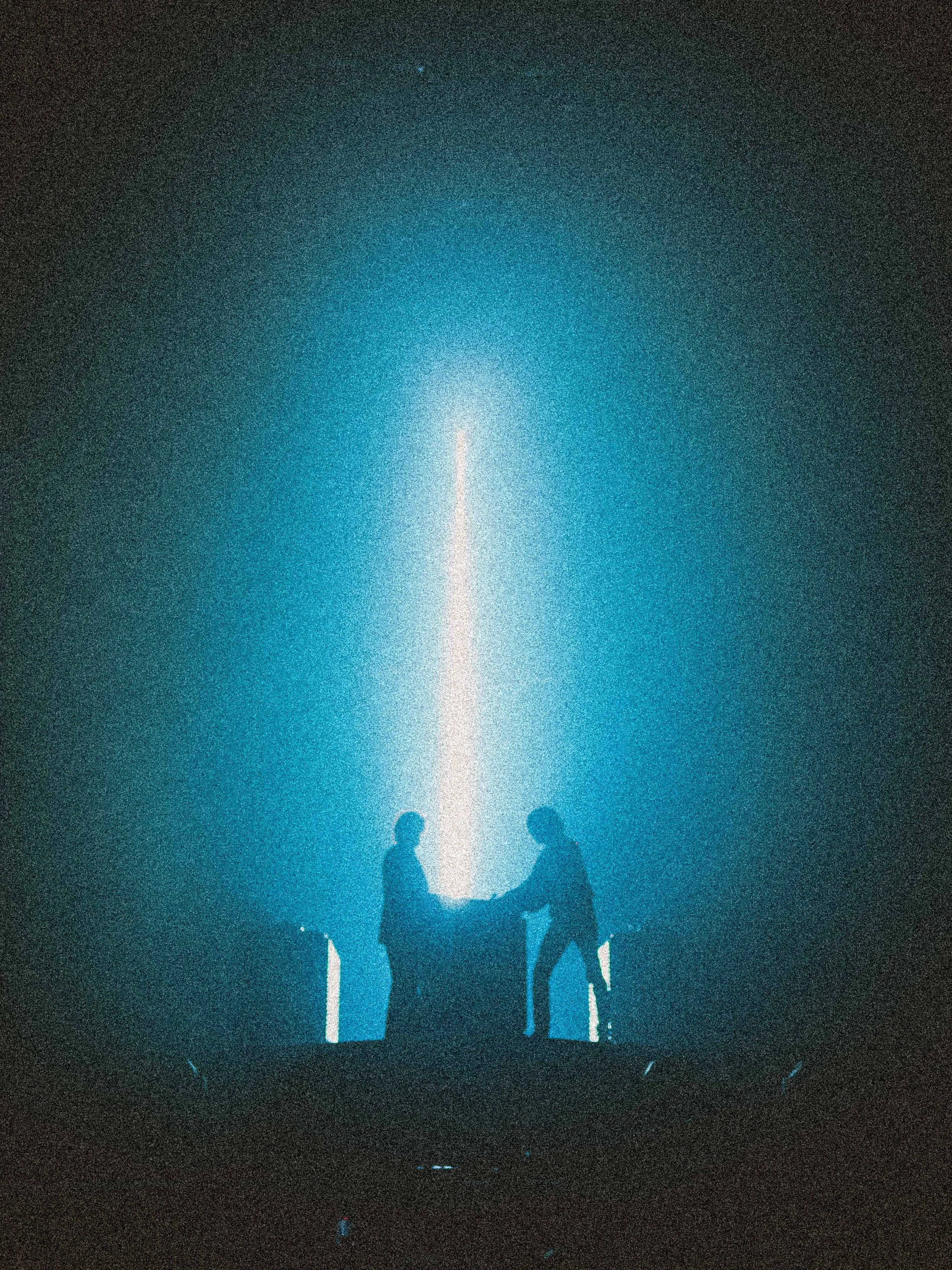 Silhouettes of three people standing and talking under a starry night sky with a bright vertical beam of light in the background.