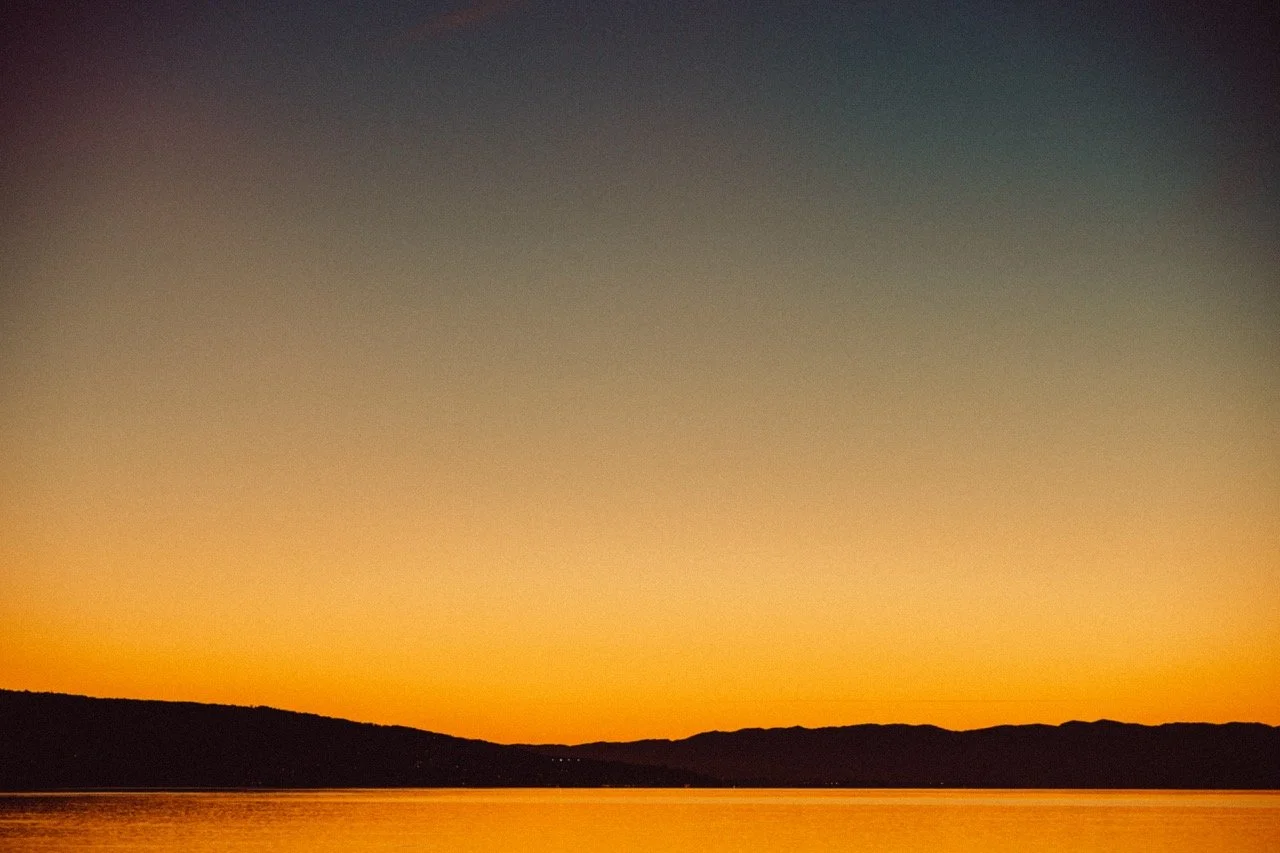 Sunset over a body of water with silhouetted hills in the distance.