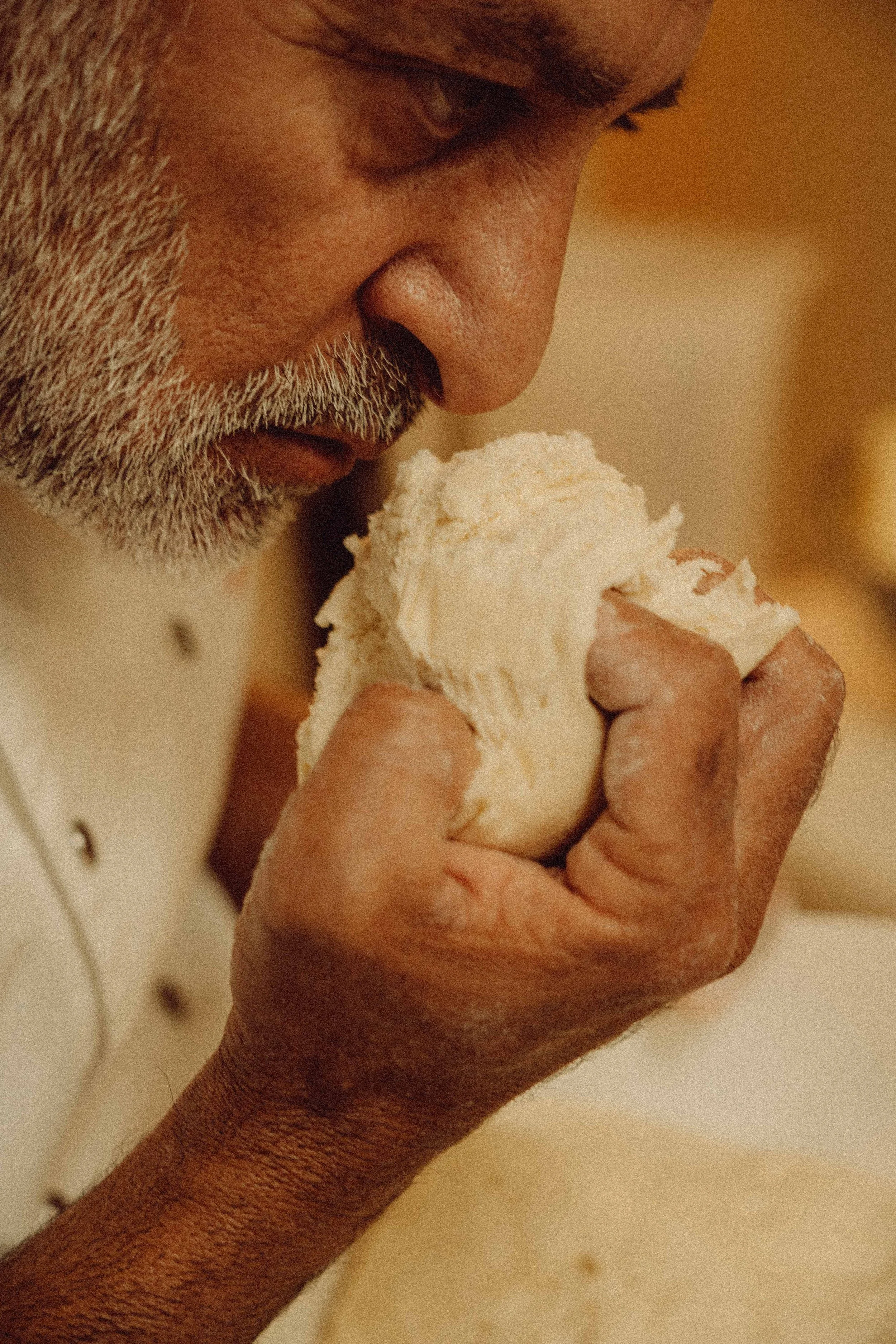 A close-up of an elderly person's face as they smell a piece of bread.