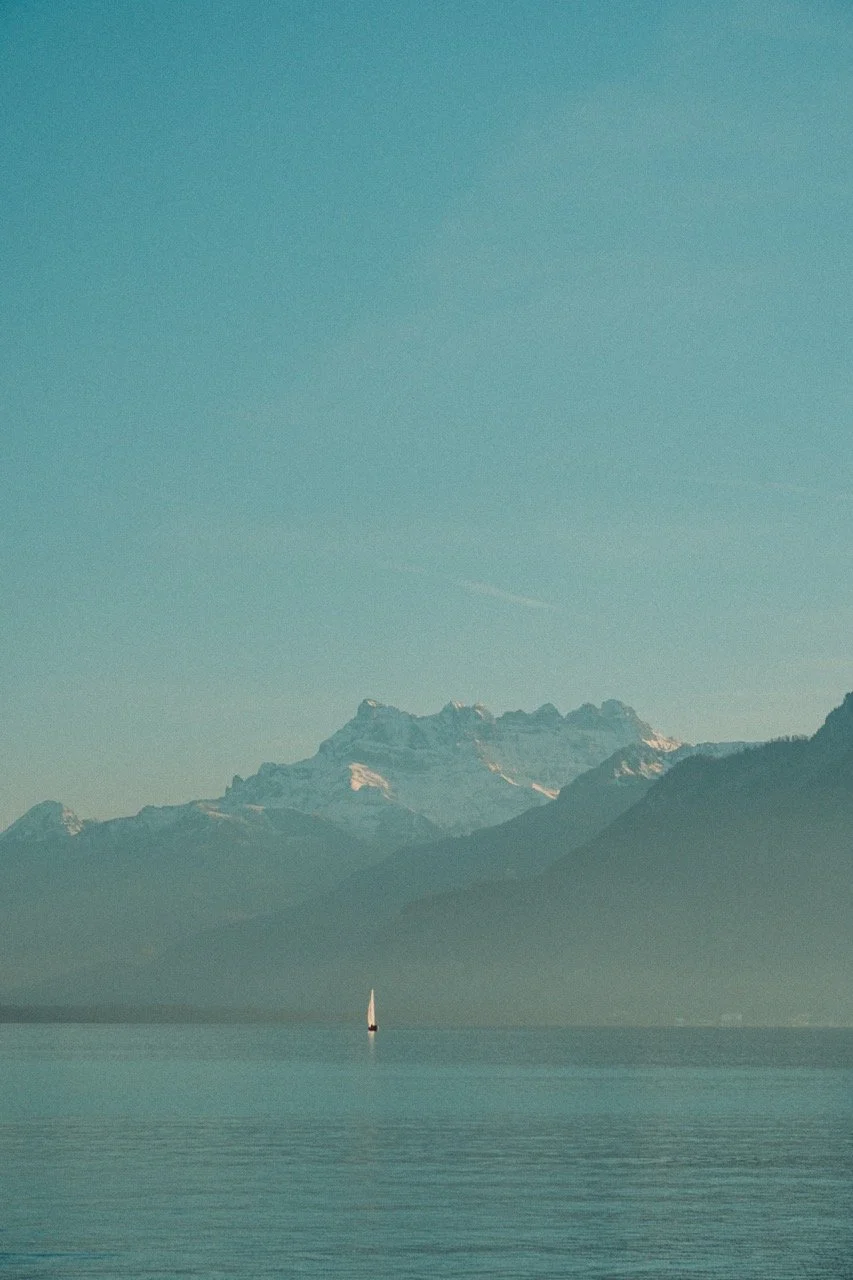 A sailboat on a calm lake with mountains in the background and a clear sky above.
