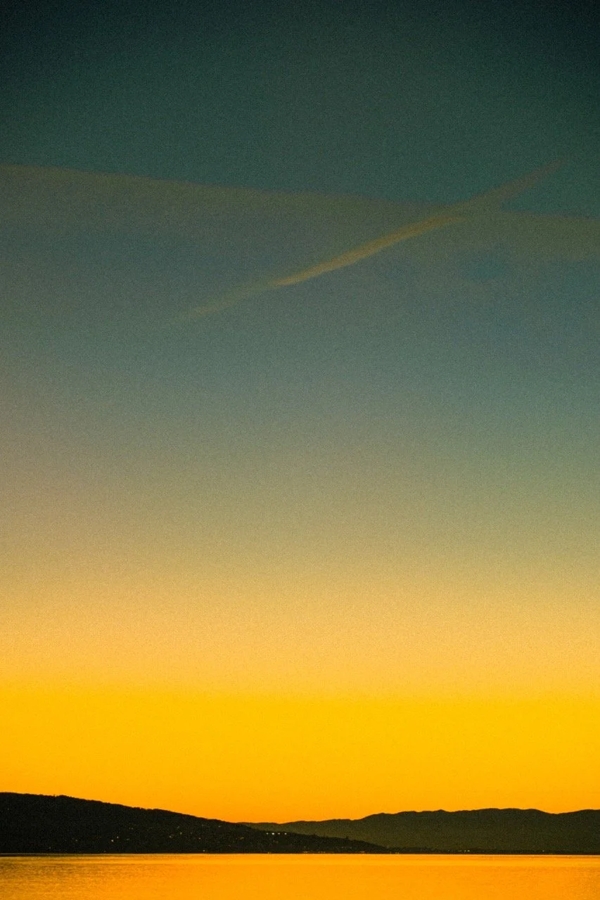 Sunset over a body of water with distant hills on the horizon.