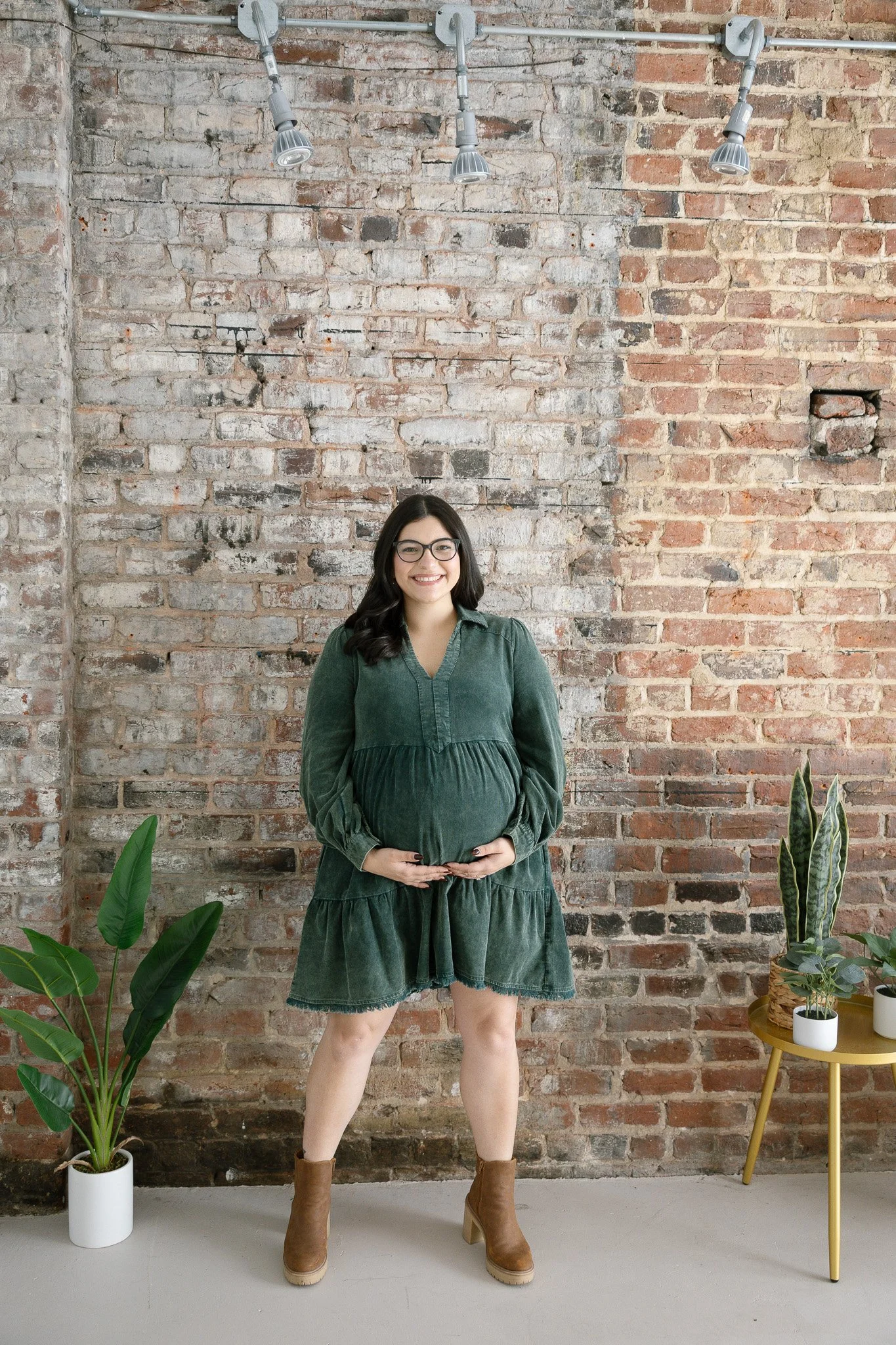 A woman wearing a short green denim maternity dress with pockets