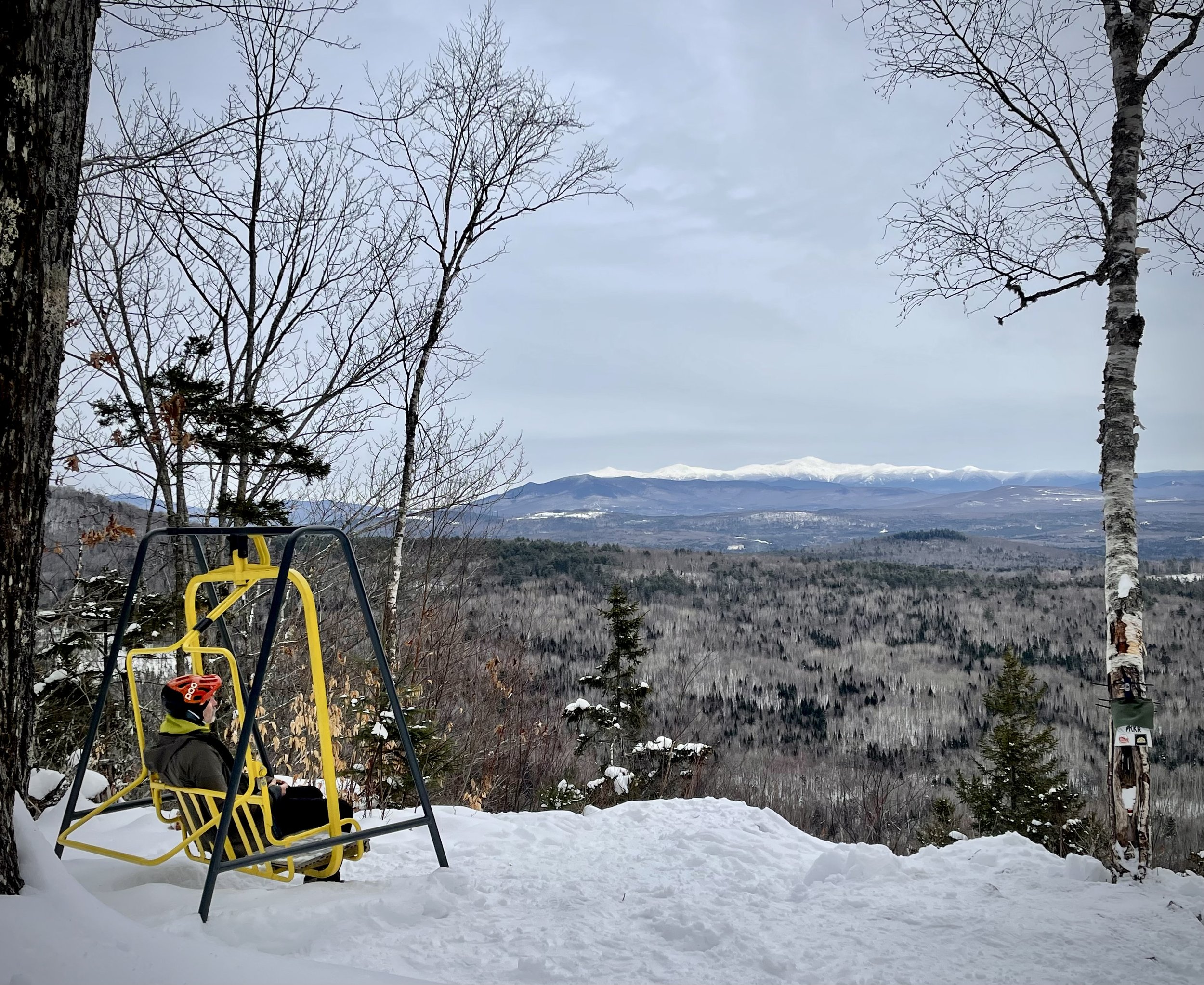 A person sitting on a bright yellow chair set on snow-covered ground at Linda's Lookout