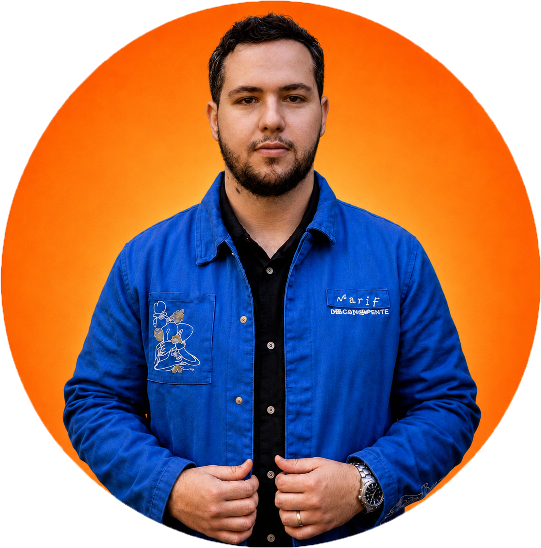A man with short dark hair and a beard, wearing a blue jacket over a black shirt, standing against an orange background.