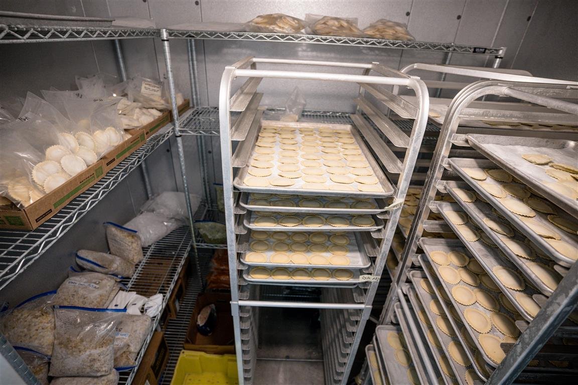 Commercial freezer with metal racks holding trays of circular pastry dough and bags of food ingredients.