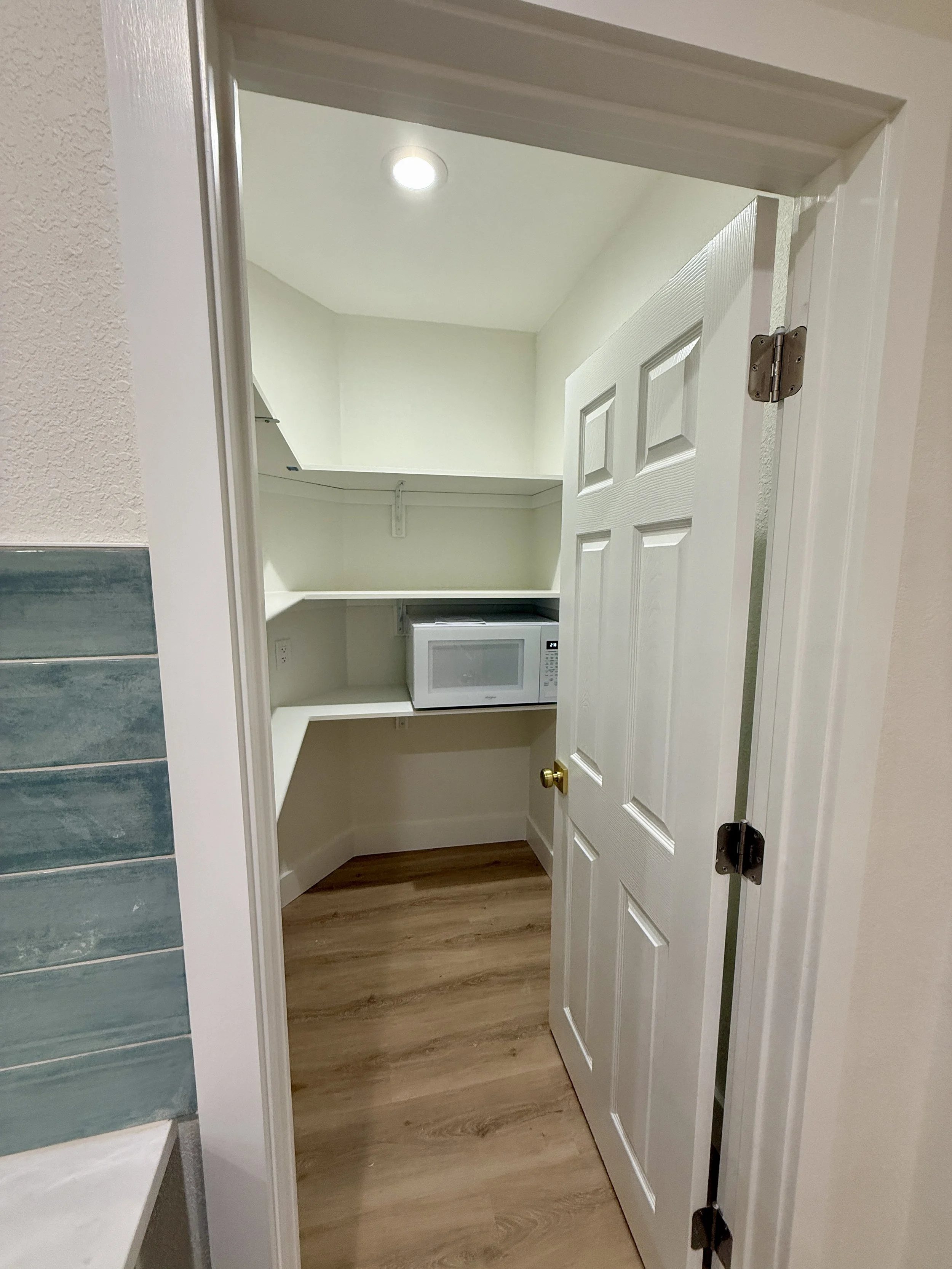 A small walk-in pantry with white shelves, a microwave, and a recessed ceiling light.
