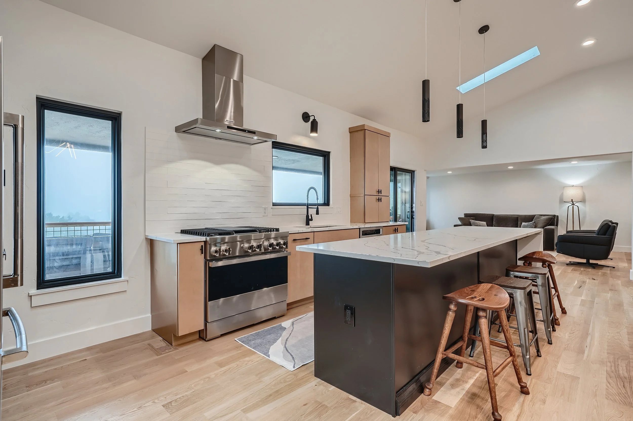 Modern open-concept kitchen with a marble island, black cabinetry, stainless steel appliances, and a living area with a sofa and armchair in the background.