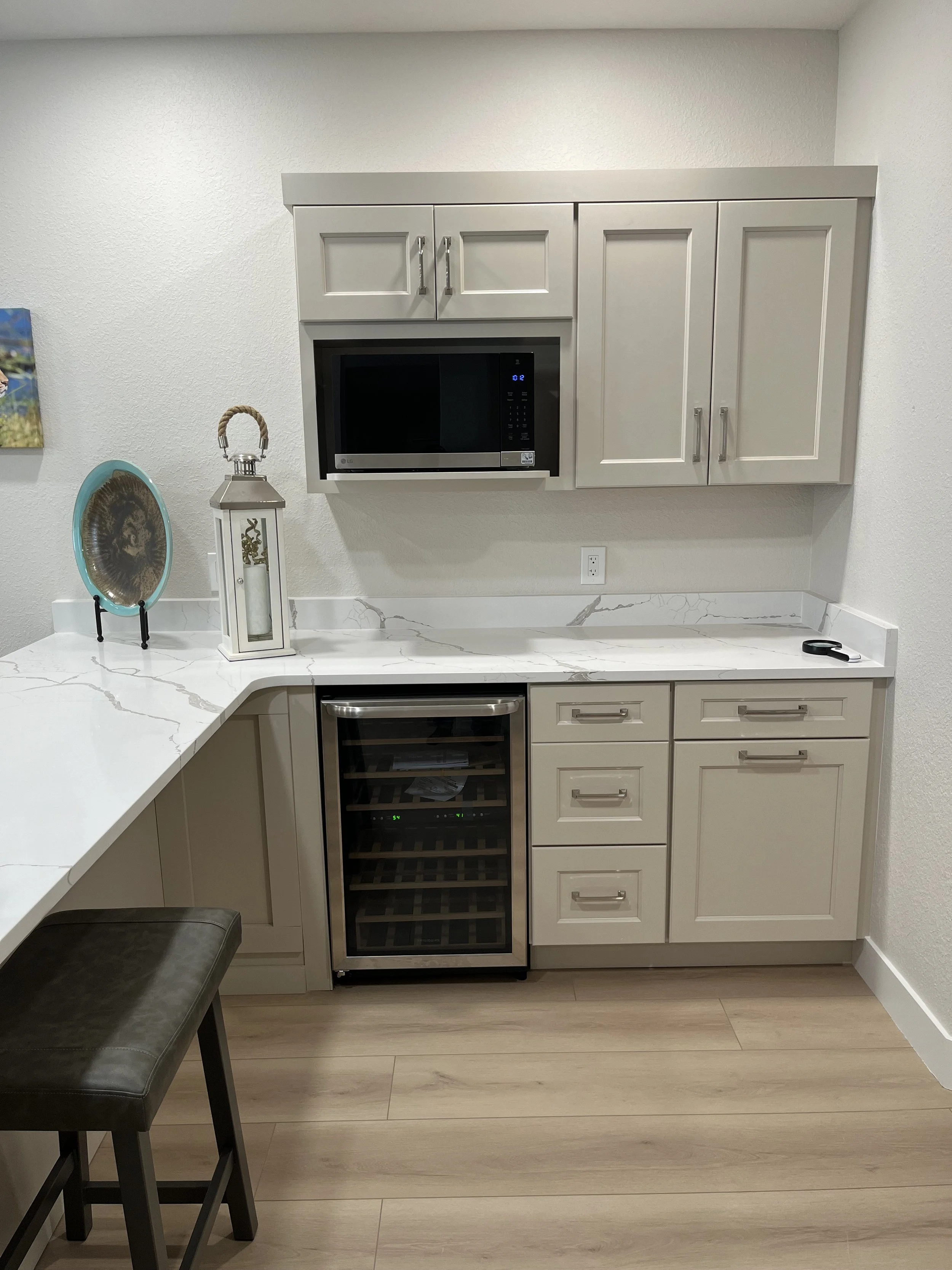 Kitchen with light gray cabinets, white marble countertop, microwave, and wine cooler.