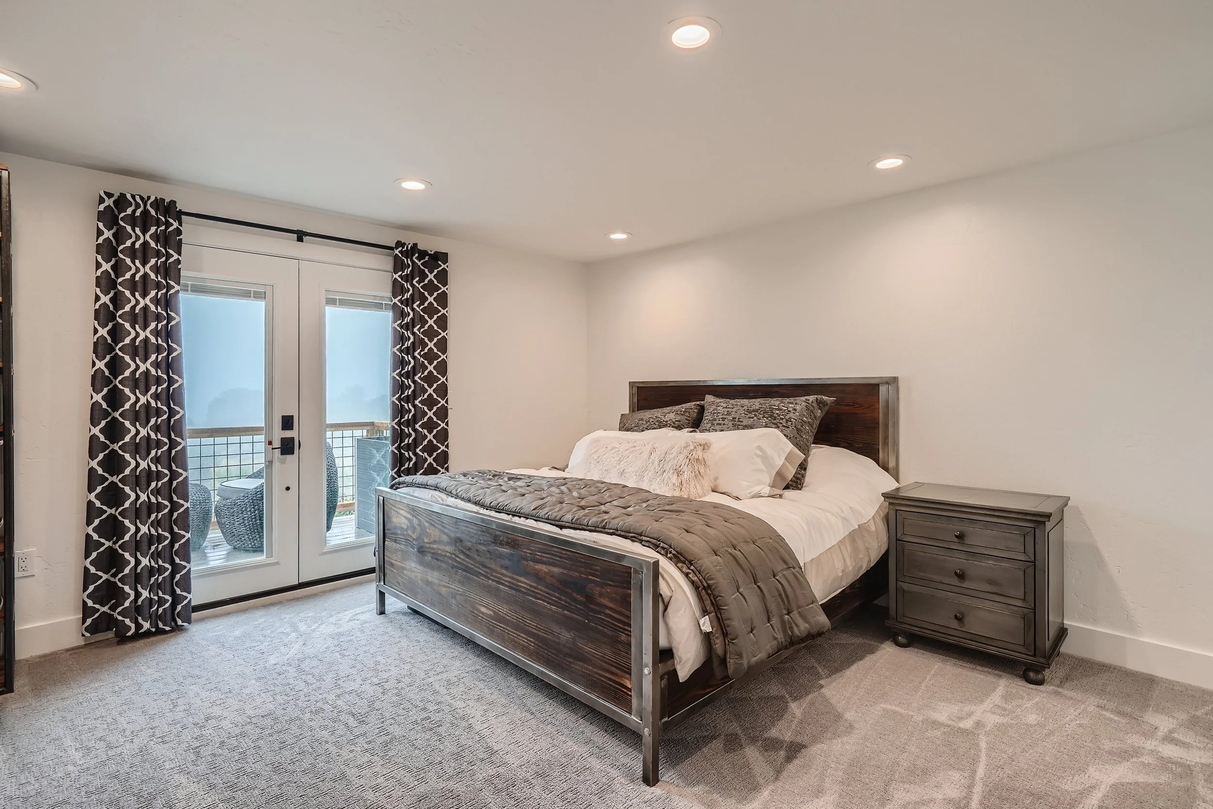 Modern bedroom with a wooden bed, gray nightstand, and patterned curtains leading to a balcony.