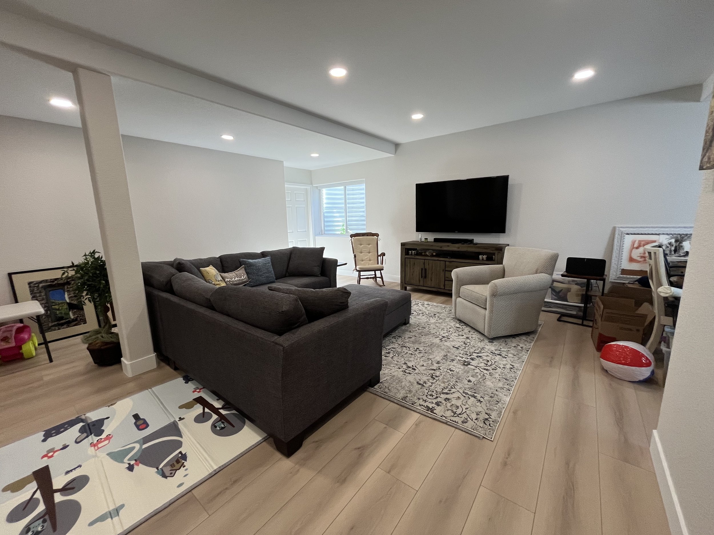 Living room with a dark sofa, an armchair, a TV mounted on the wall, and various decorative and personal items.
