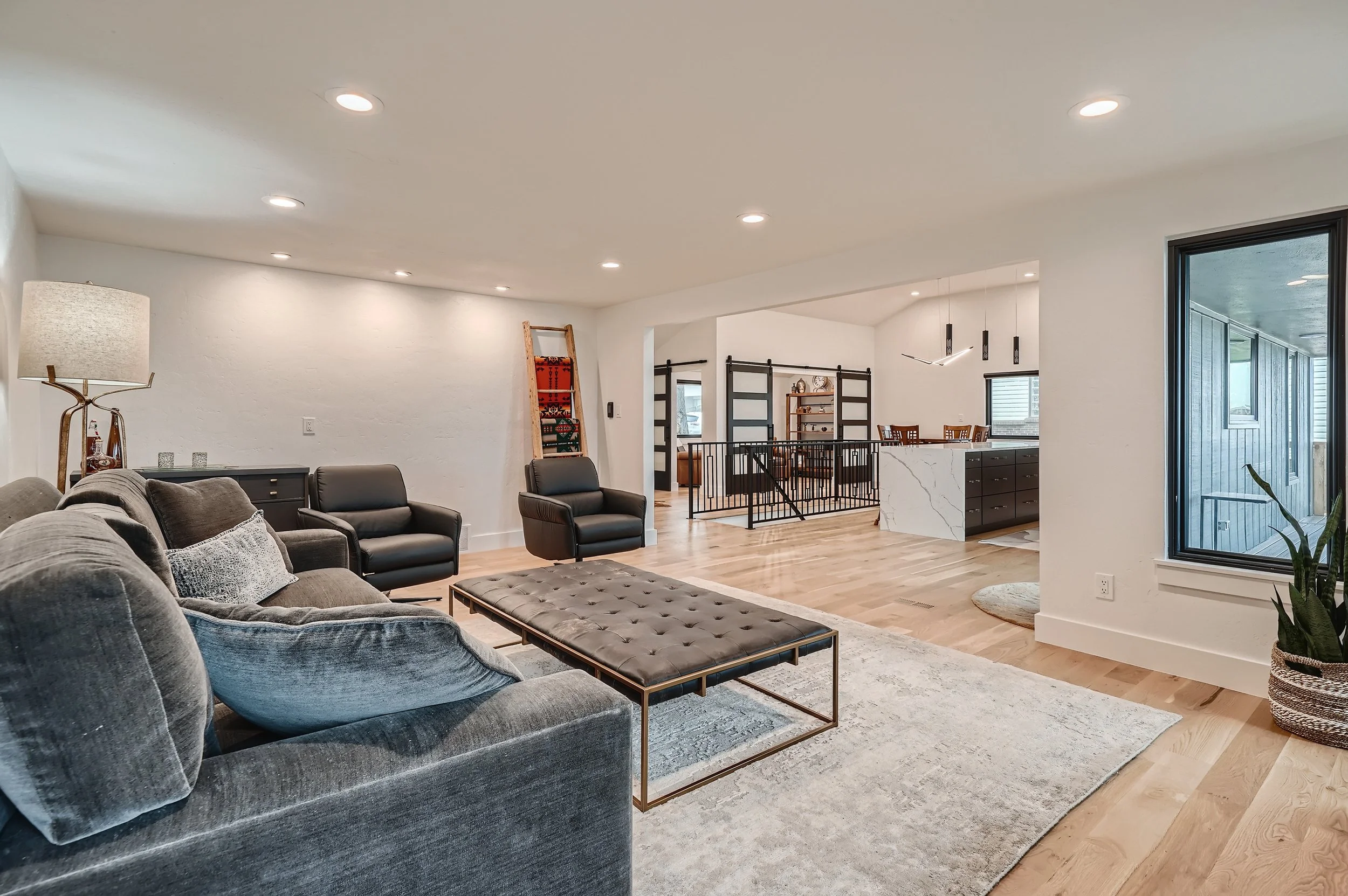 Open living room with gray sofa, black armchairs, wooden floor, white walls, and modern decor