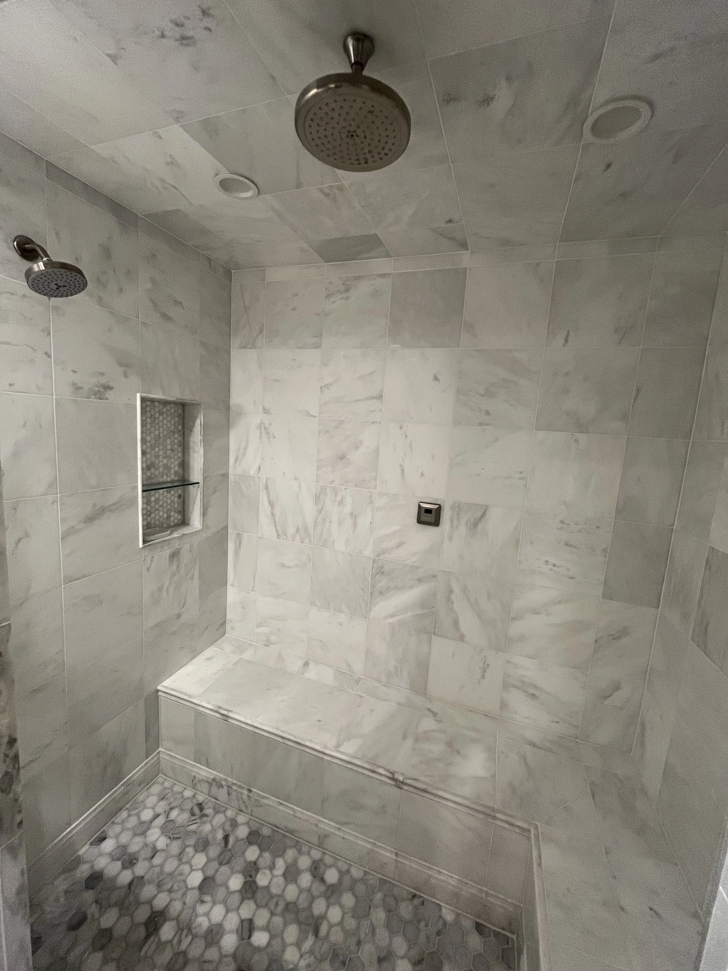 Marble tiled shower with two showerheads, a built-in niche with glass shelf, and a marble bench.