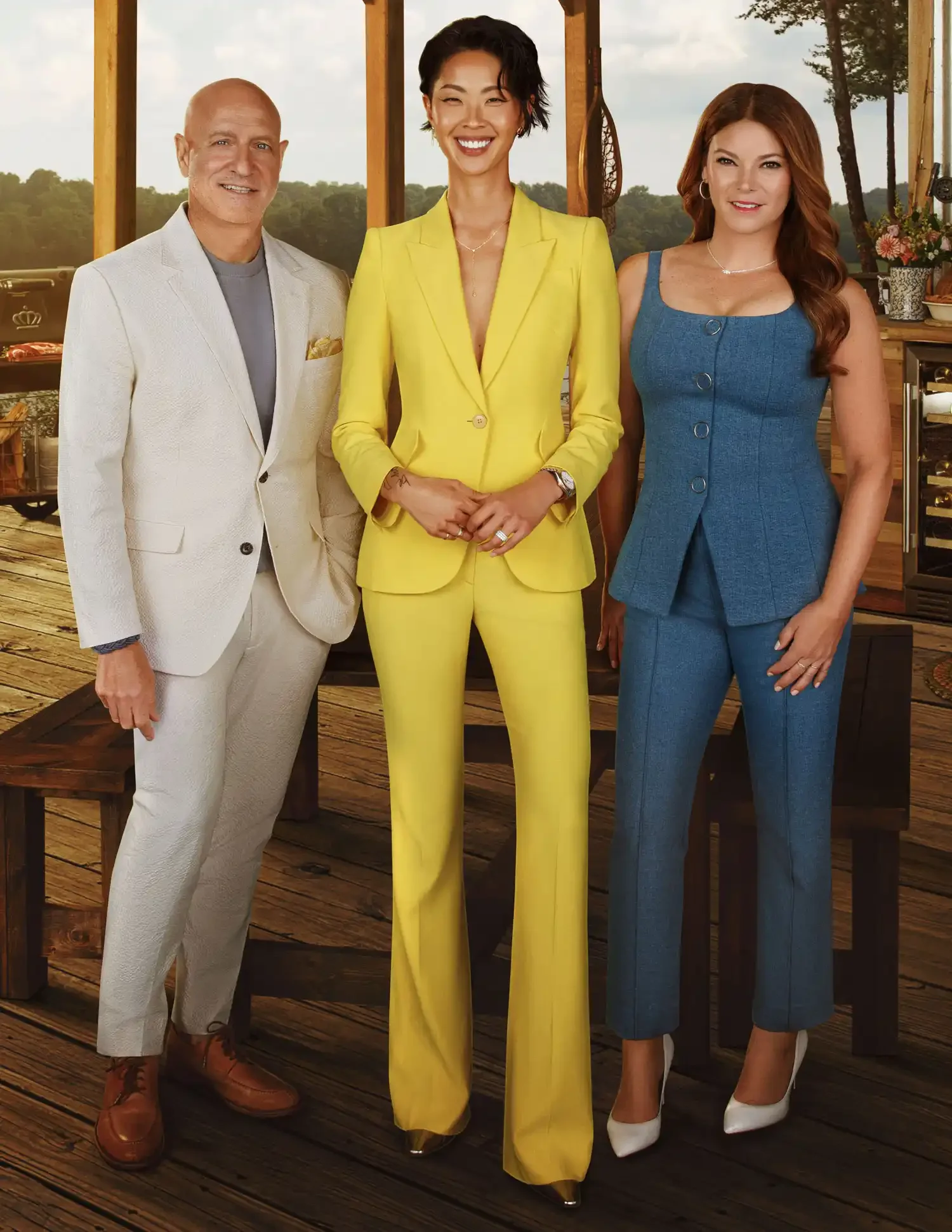 Three people standing together on a wooden deck, dressed in colorful suits, with a natural outdoor background and trees visible through large windows.