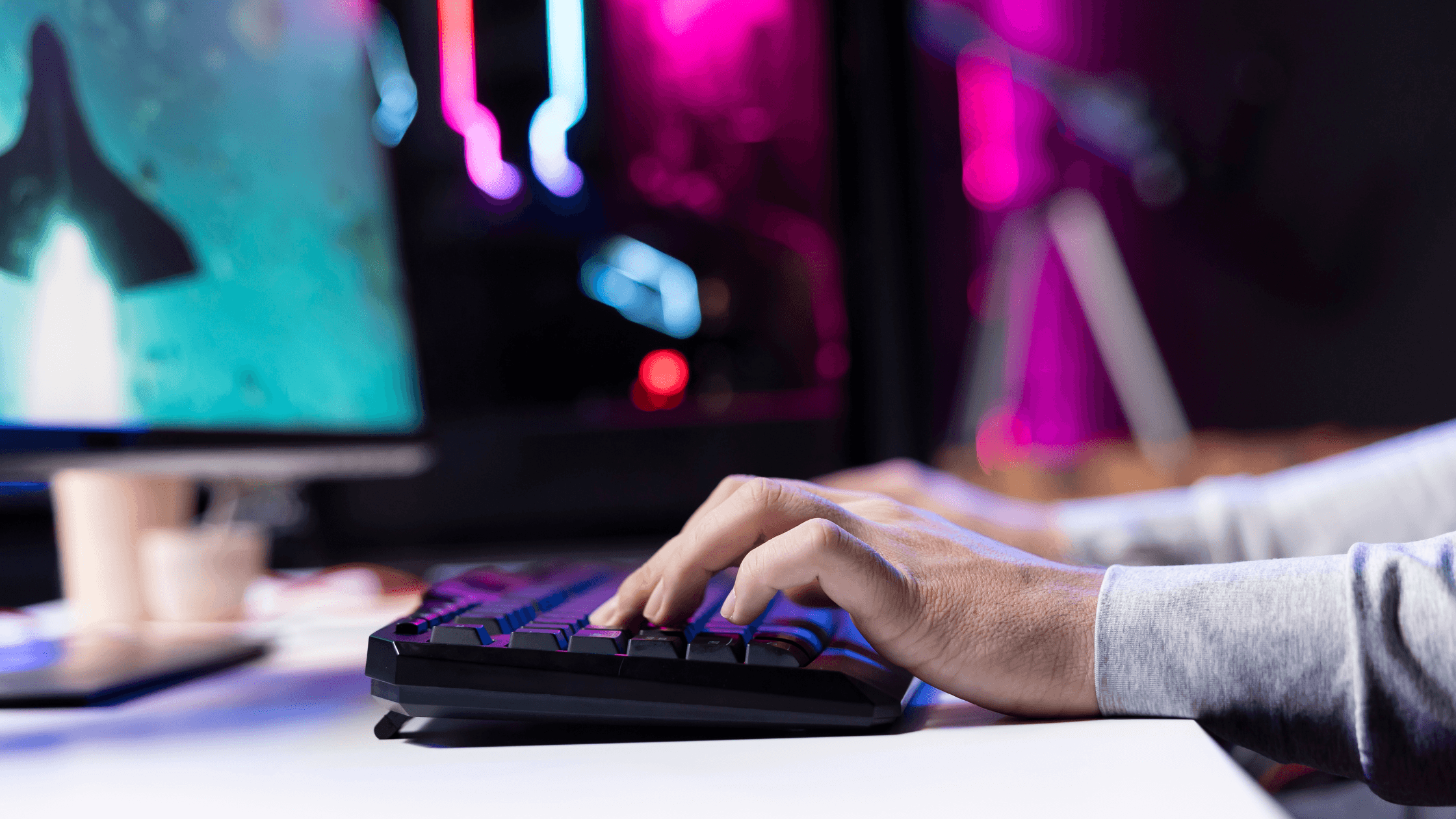 Person typing on a gaming keyboard with animated screens displaying colorful lights and graphics in the background.