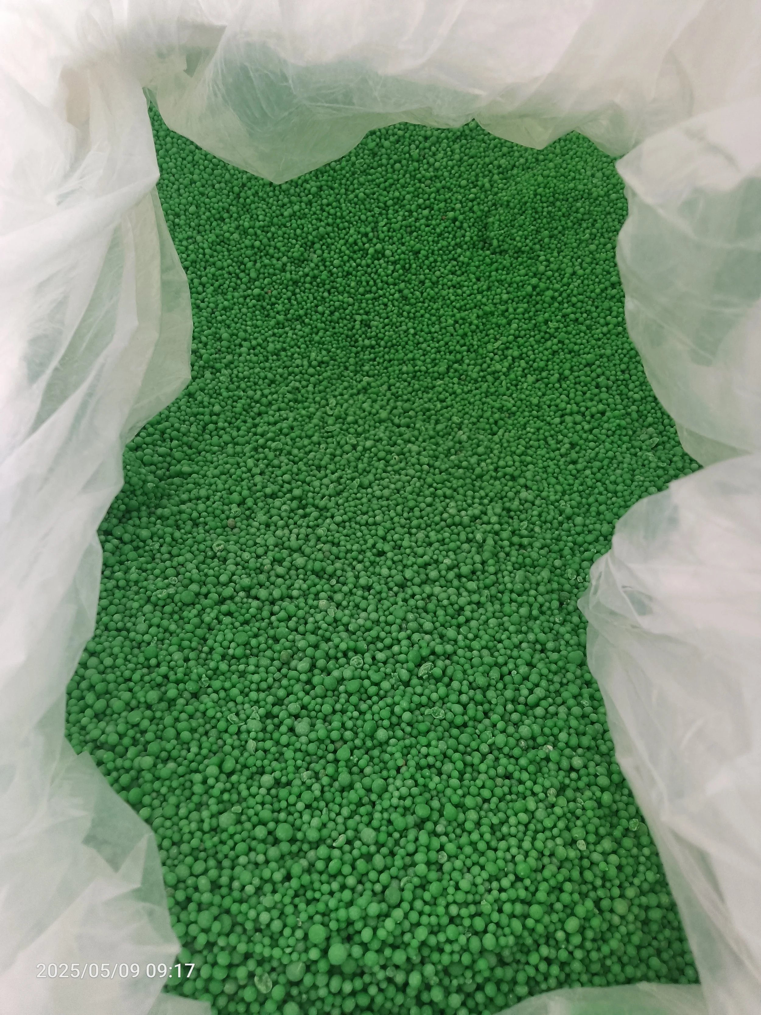 Close-up of green plastic pellets inside a white plastic bag.
