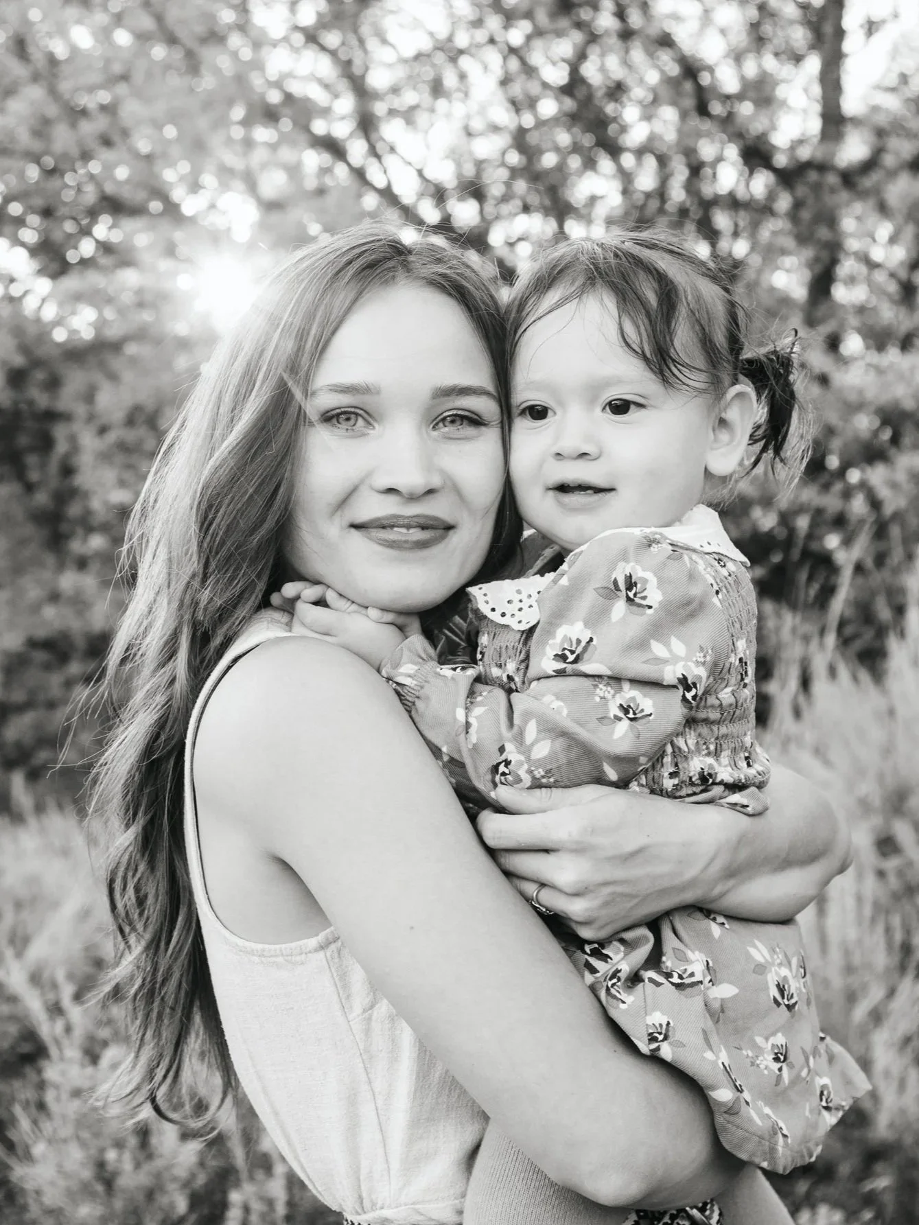 A woman holding a young girl outdoors with trees in the background, black and white photo.