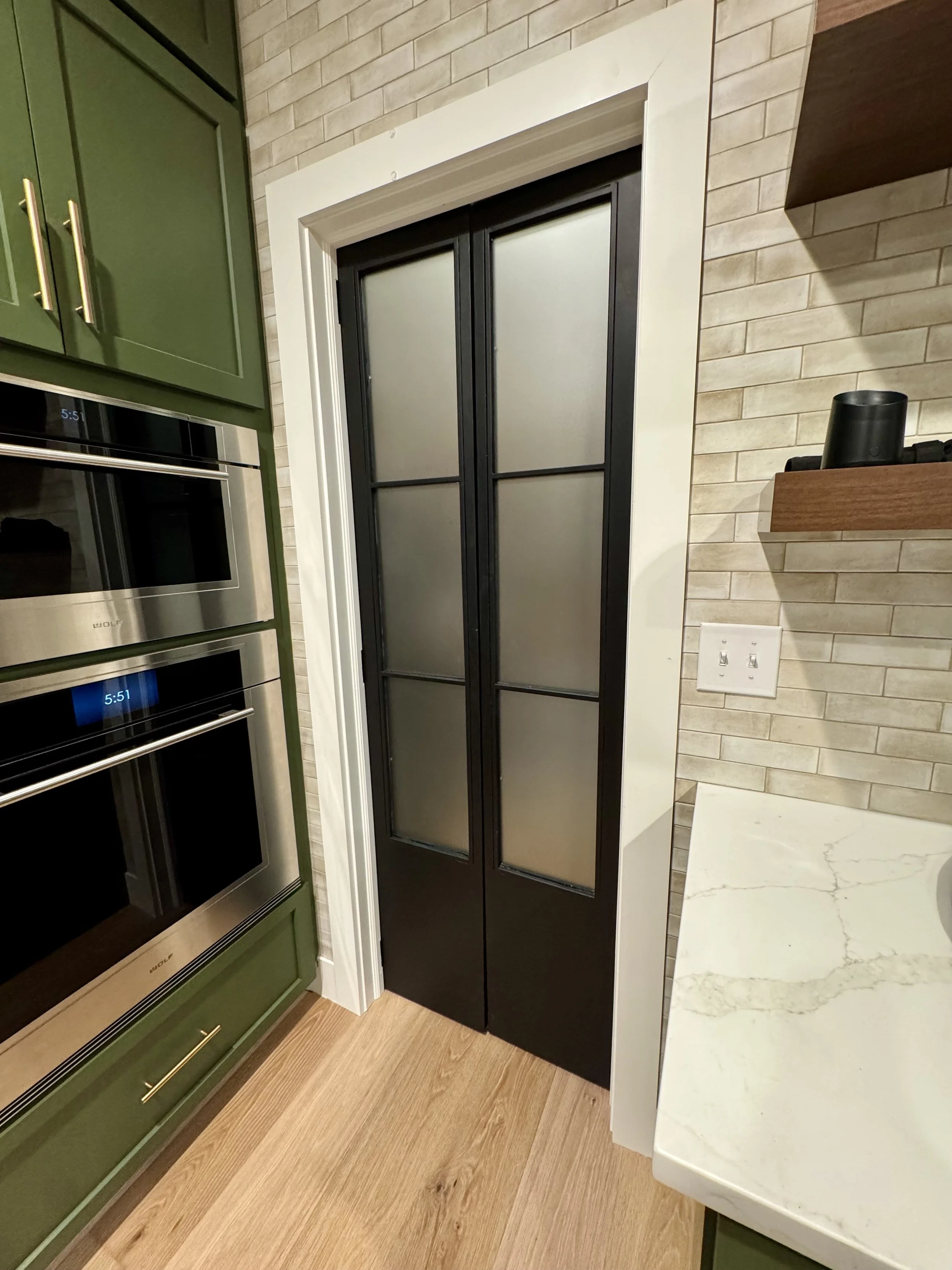 Kitchen with green cabinets, and a black sliding door with frosted glass panels next to a white countertop.