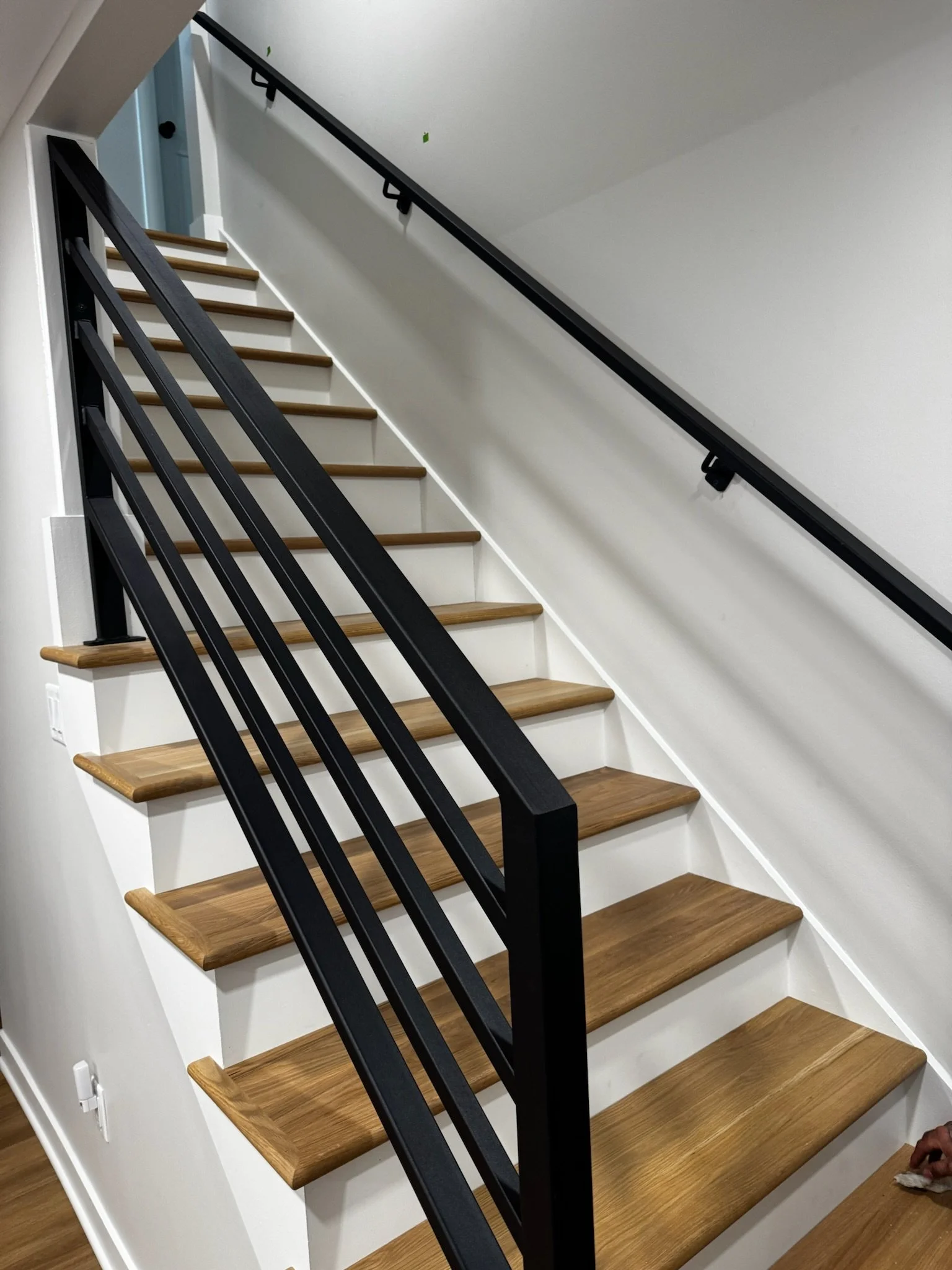 Photo of a modern staircase with wooden steps, white risers, black metal railing, and a white wall.