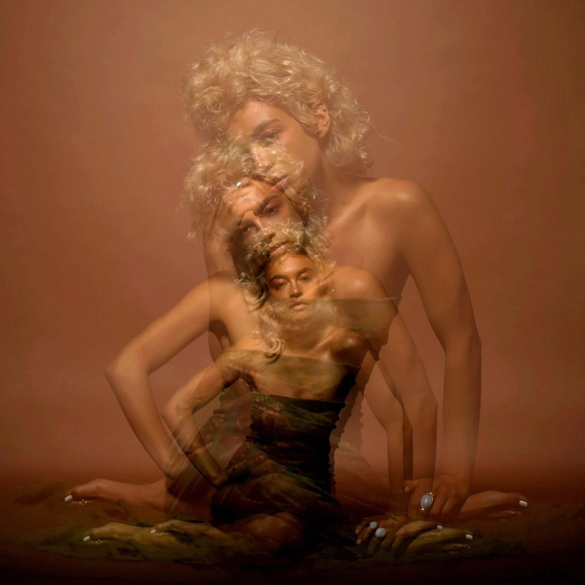 A woman with curly blond hair and rings on her fingers is posing with her hand on her head against a brown background, creating a layered, abstract effect.