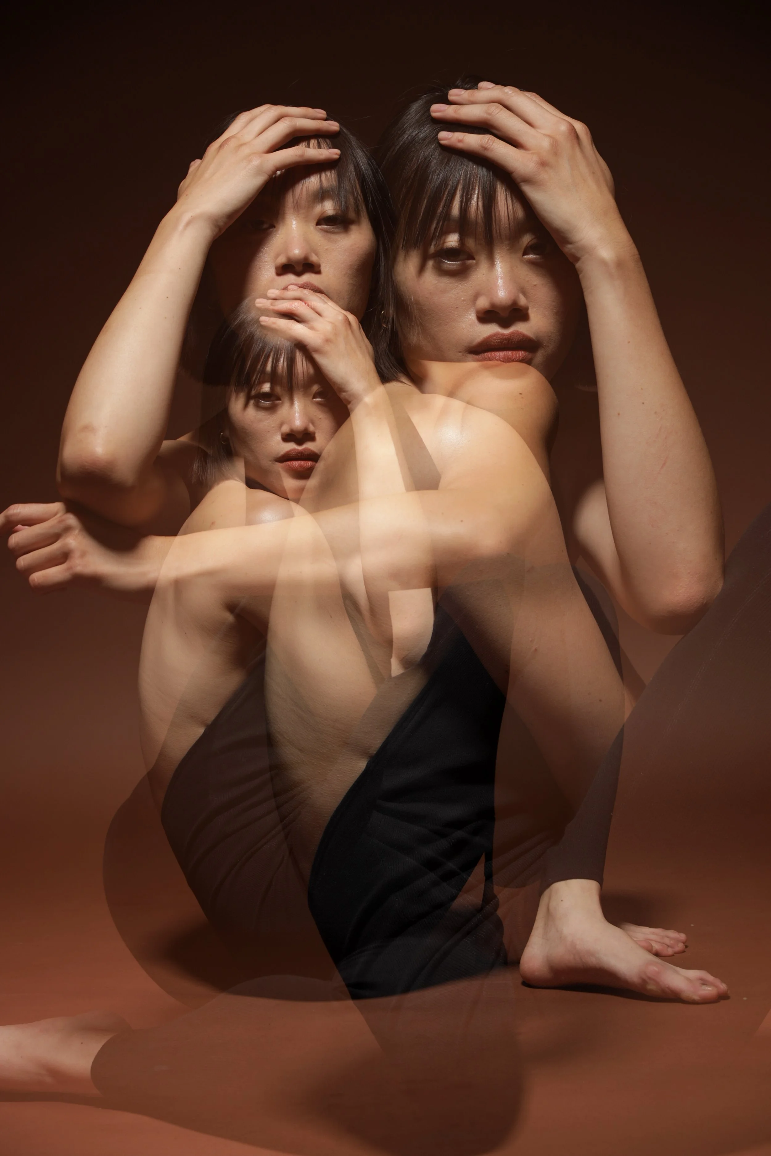 A woman with short black hair in a black outfit is performing a yoga pose on the floor, with a brown background and multiple layered images creating a layered effect.