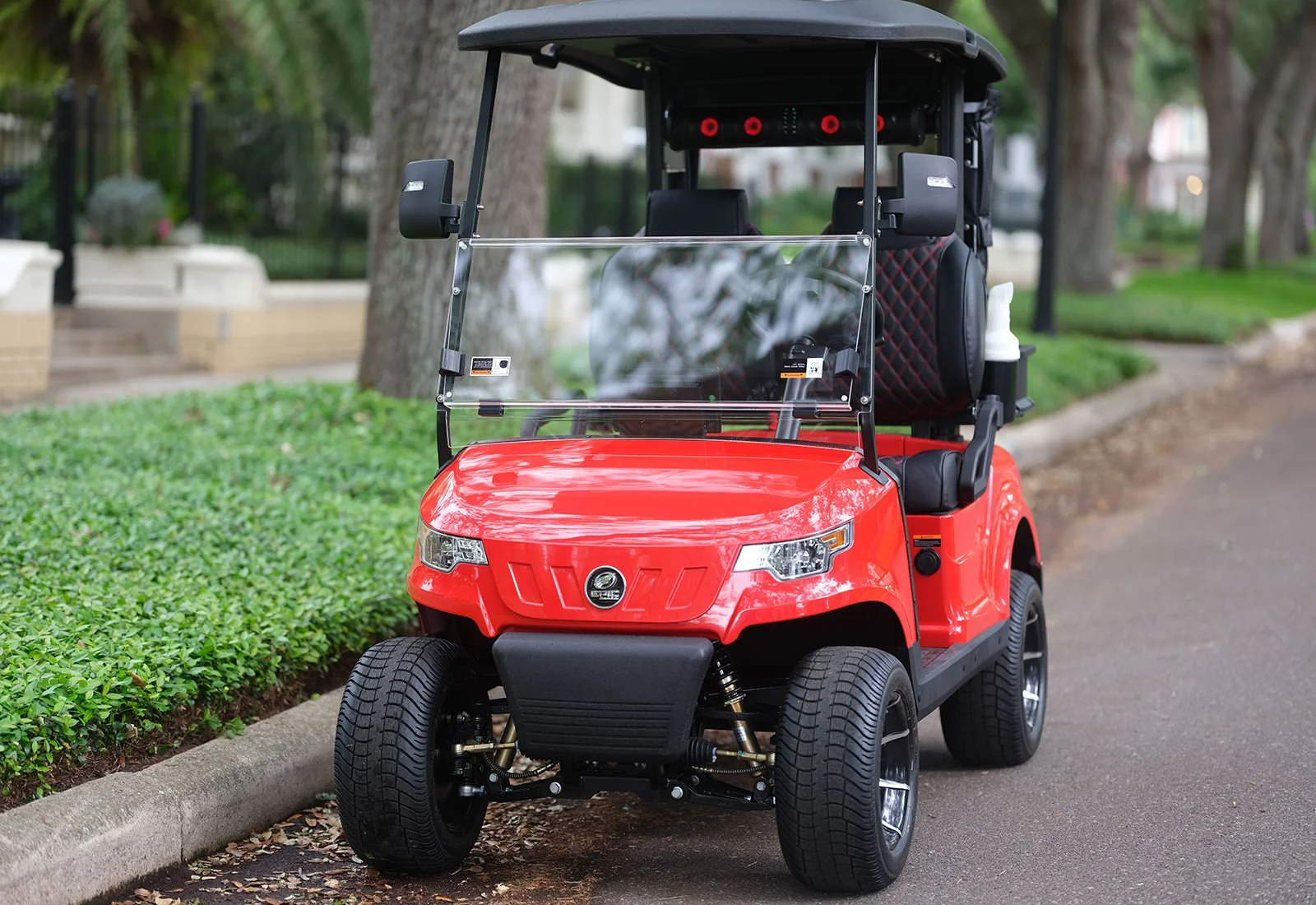Red golf cart parked on a residential street with trees and greenery in the background.