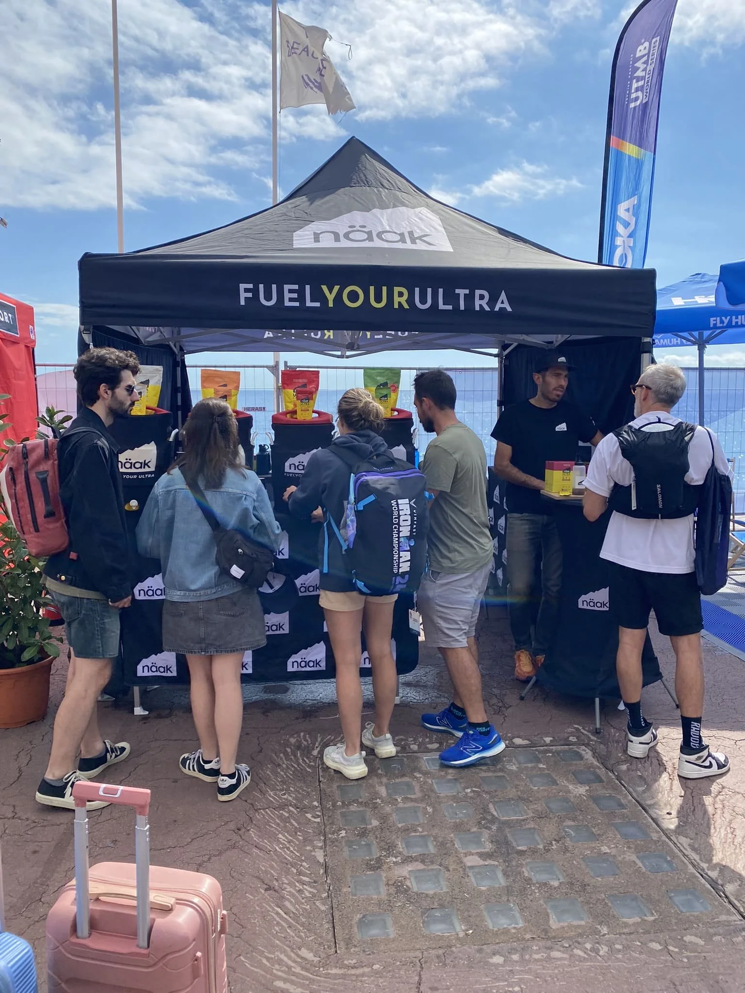 Groupe de personnes en ligne dans un stand promotionnel pour Näak, une marque de nutrition sportive, sous une tente avec le texte 'Fuel Your Ultra'.