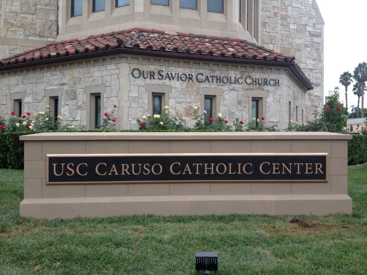 Custom campus signage identifying the USC Caruso Catholic Center with dimensional metal lettering and a monument sign.