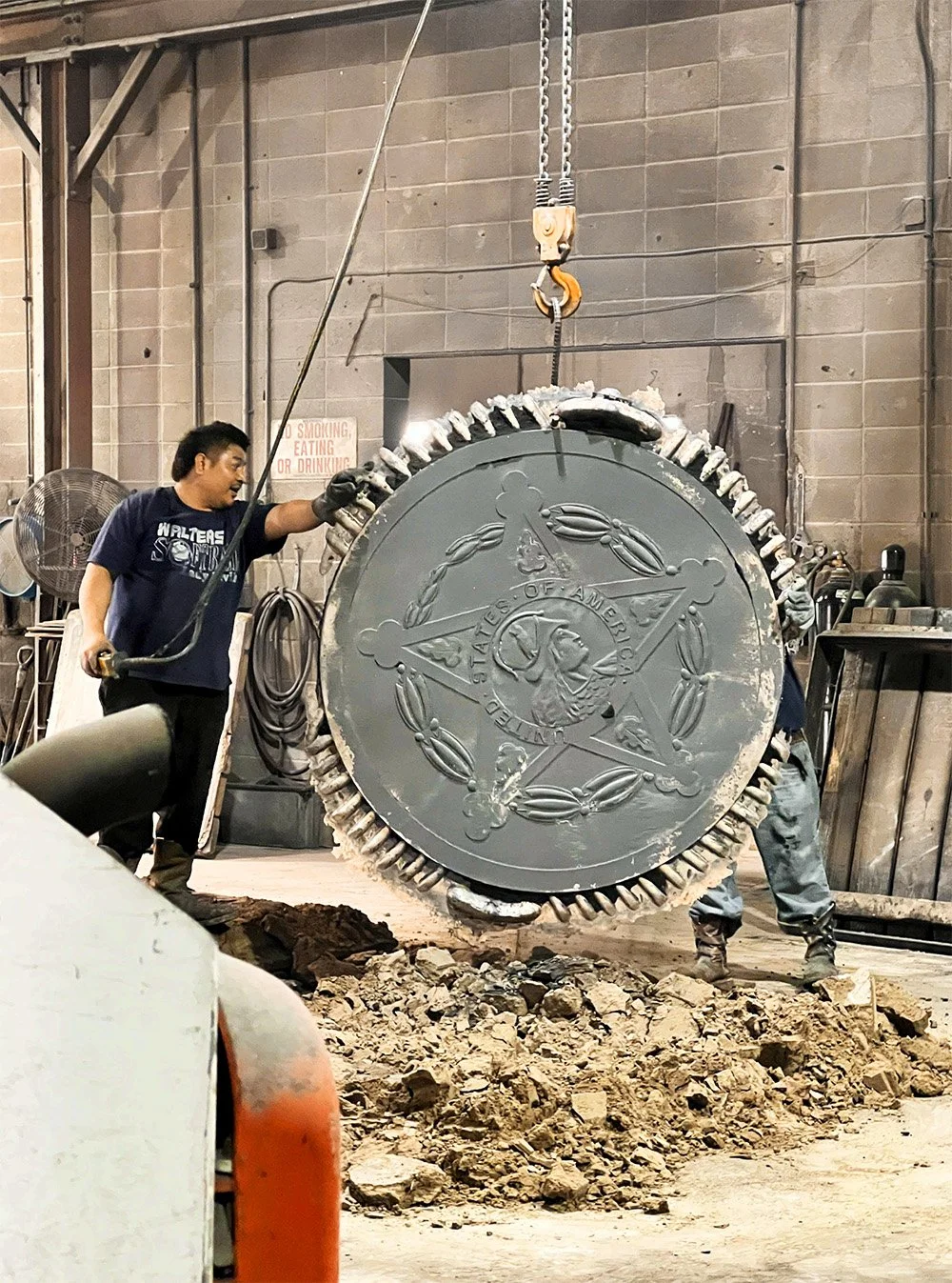 American manufacturing process showing workers handling a large custom metal casting with a United States emblem inside a metal foundry.