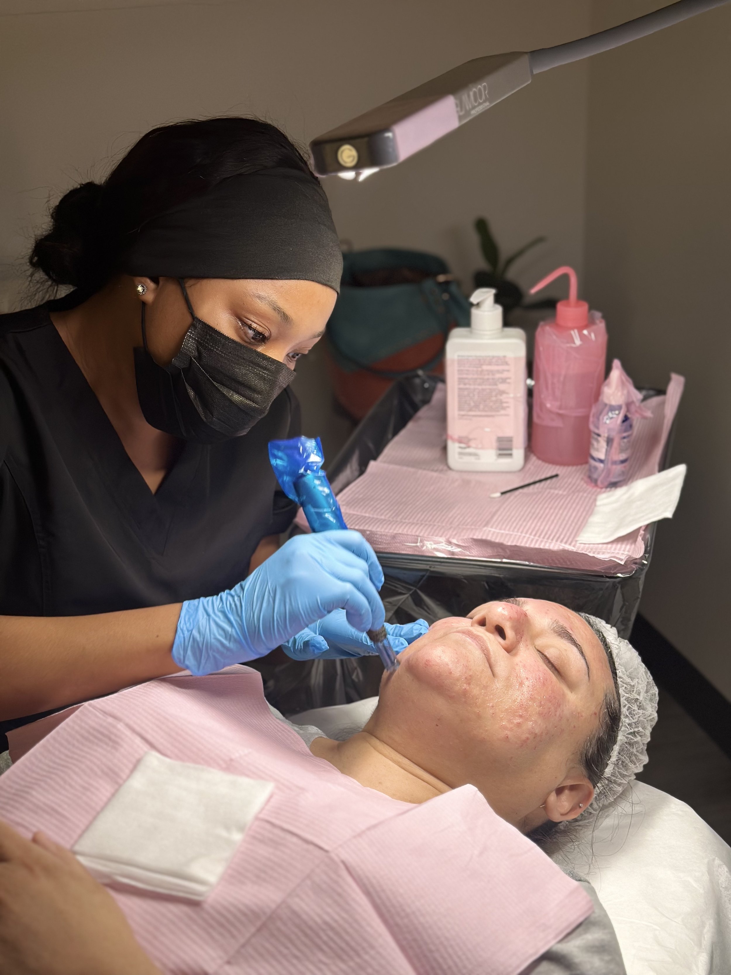 A woman receiving a facial treatment from a skincare professional in a clinic, with skincare products on a nearby table.