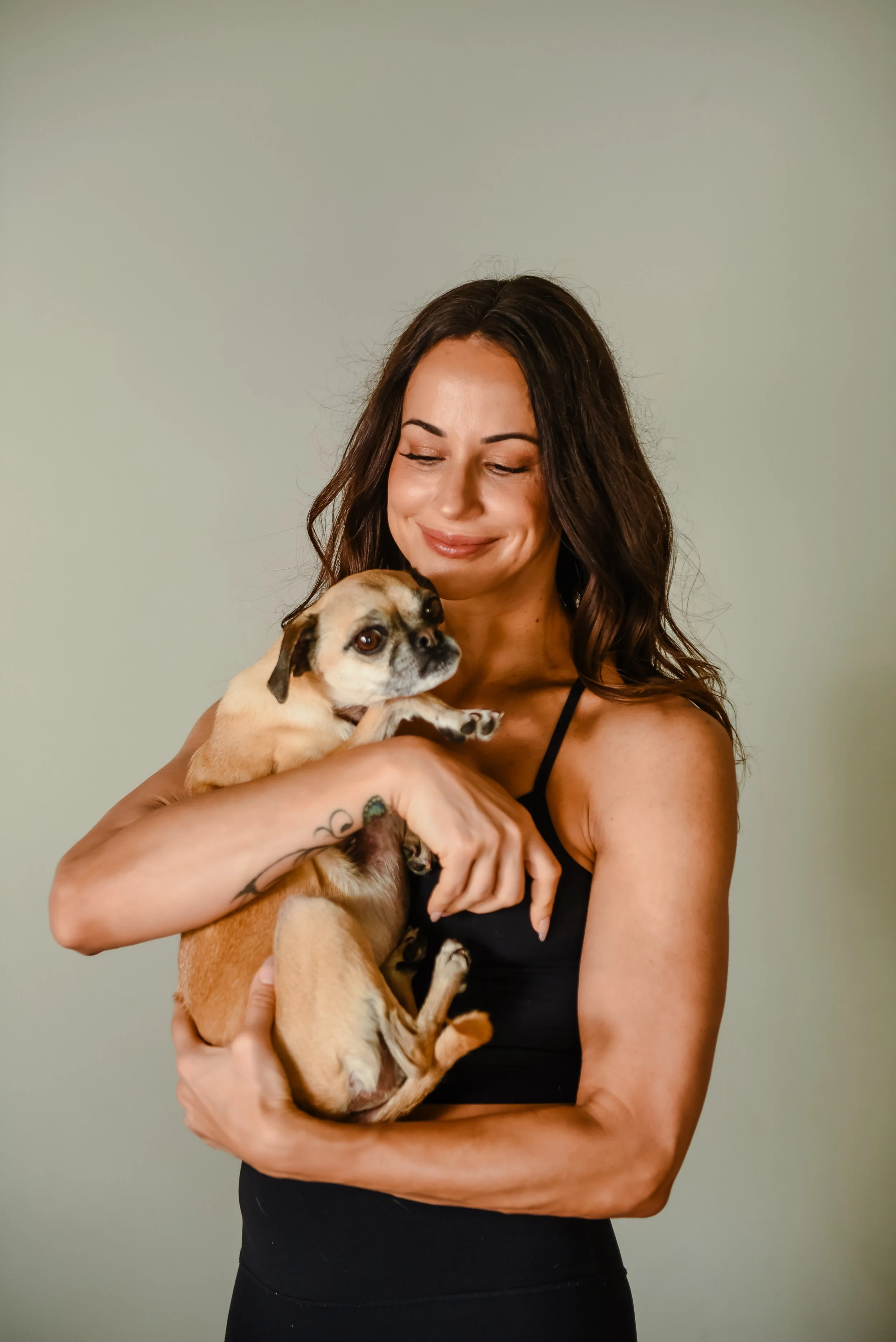 Smiling woman with wavy blond hair holding a small pug dog.